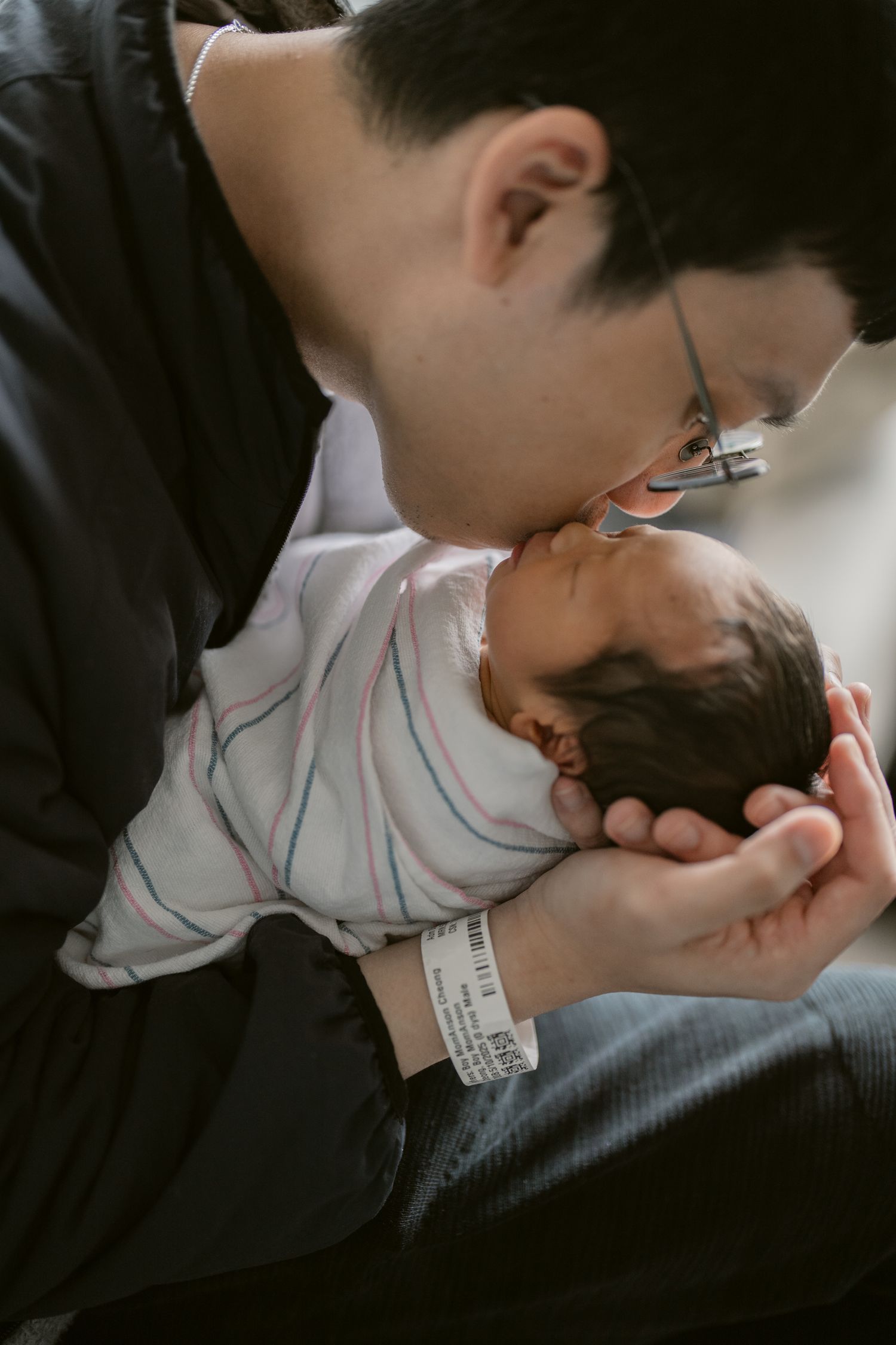 Parent gently kissing newborn wrapped in striped hospital blanket.