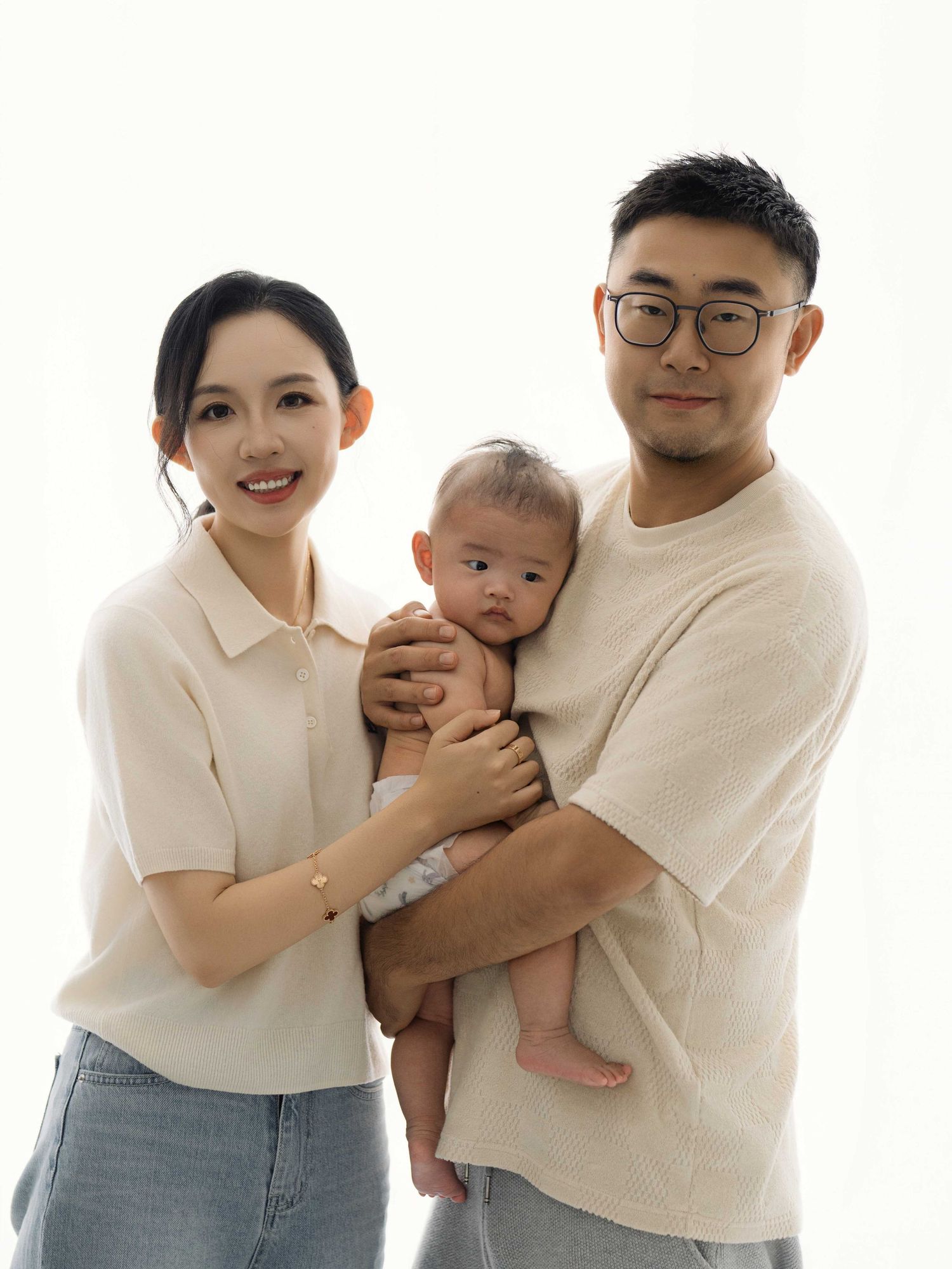 Family portrait with parents holding baby in matching cream colored outfits.
