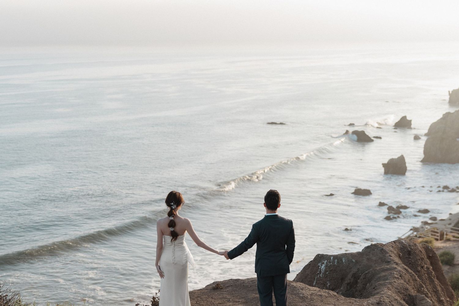 Romantic wedding photography session on dramatic oceanside cliff at sunset.