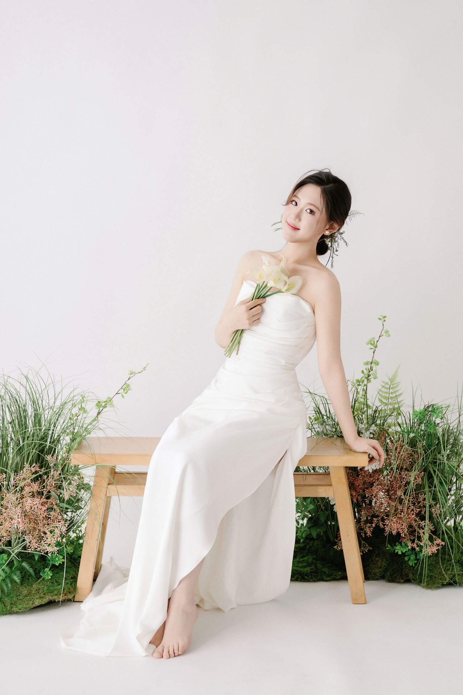 Dreamy bridal portraits on wooden bench with lush green botanical backdrop.