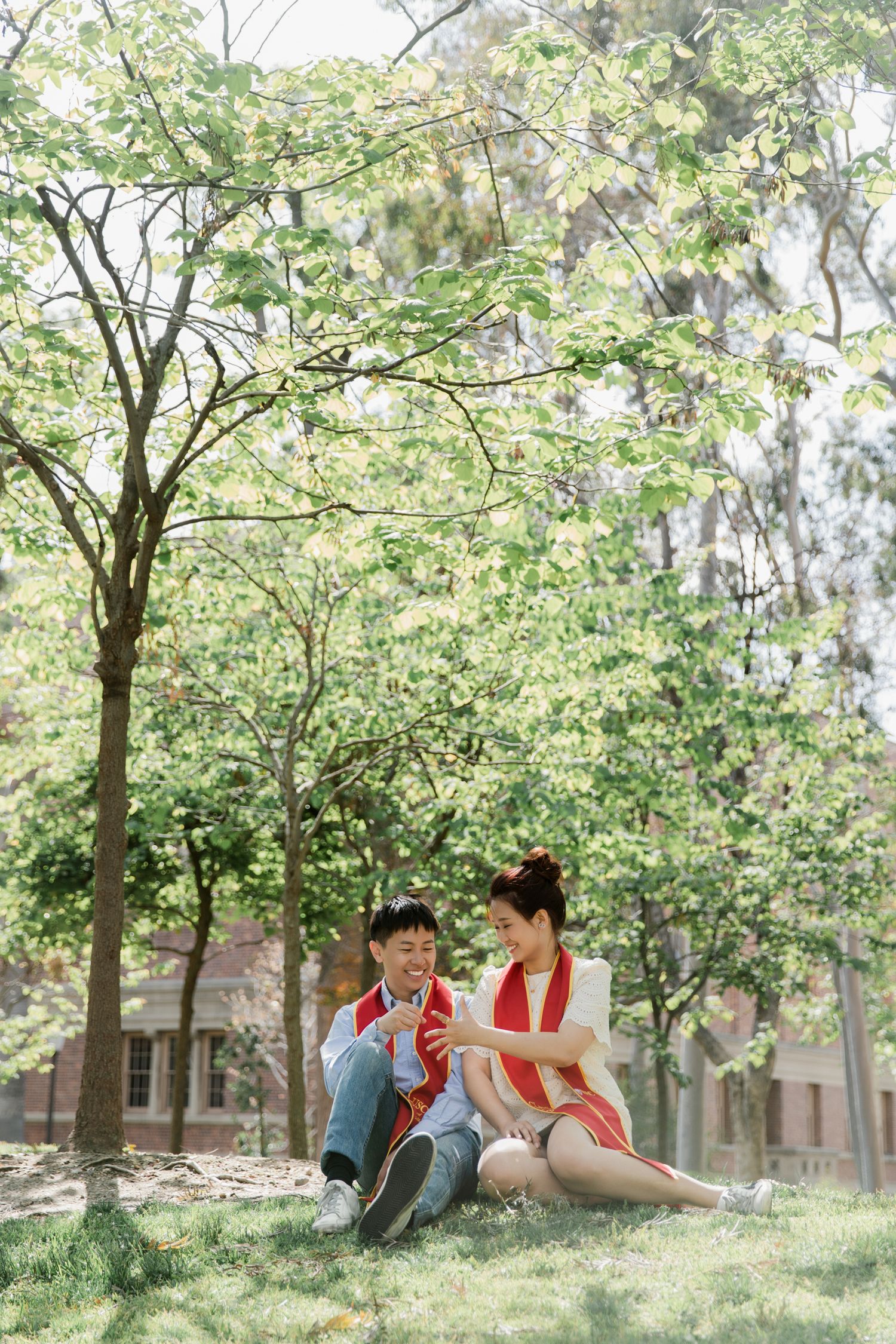 Couple relaxing together on grass under green trees in a park setting.