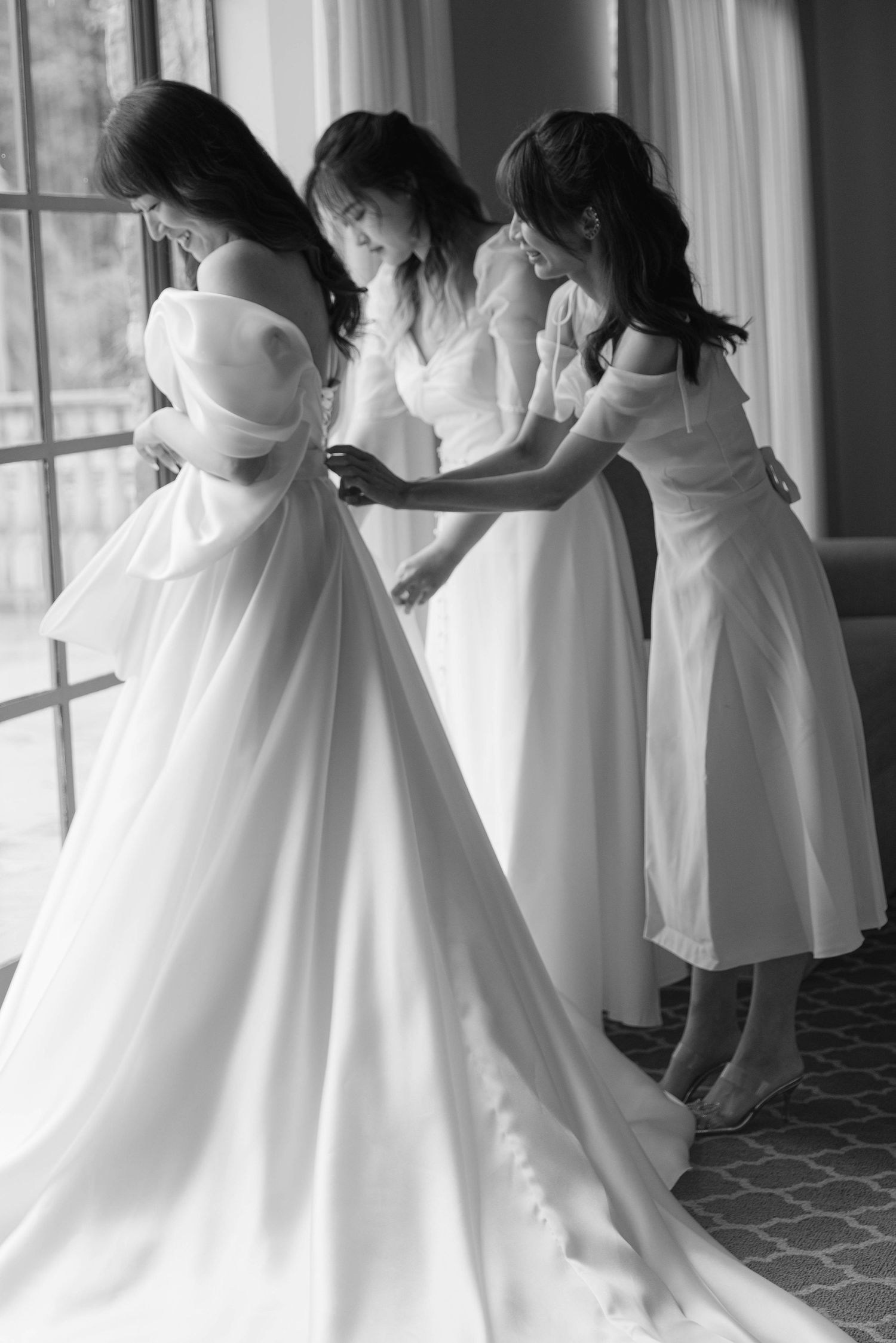 Black and white photo of flowing white wedding dresses in motion near large windows.