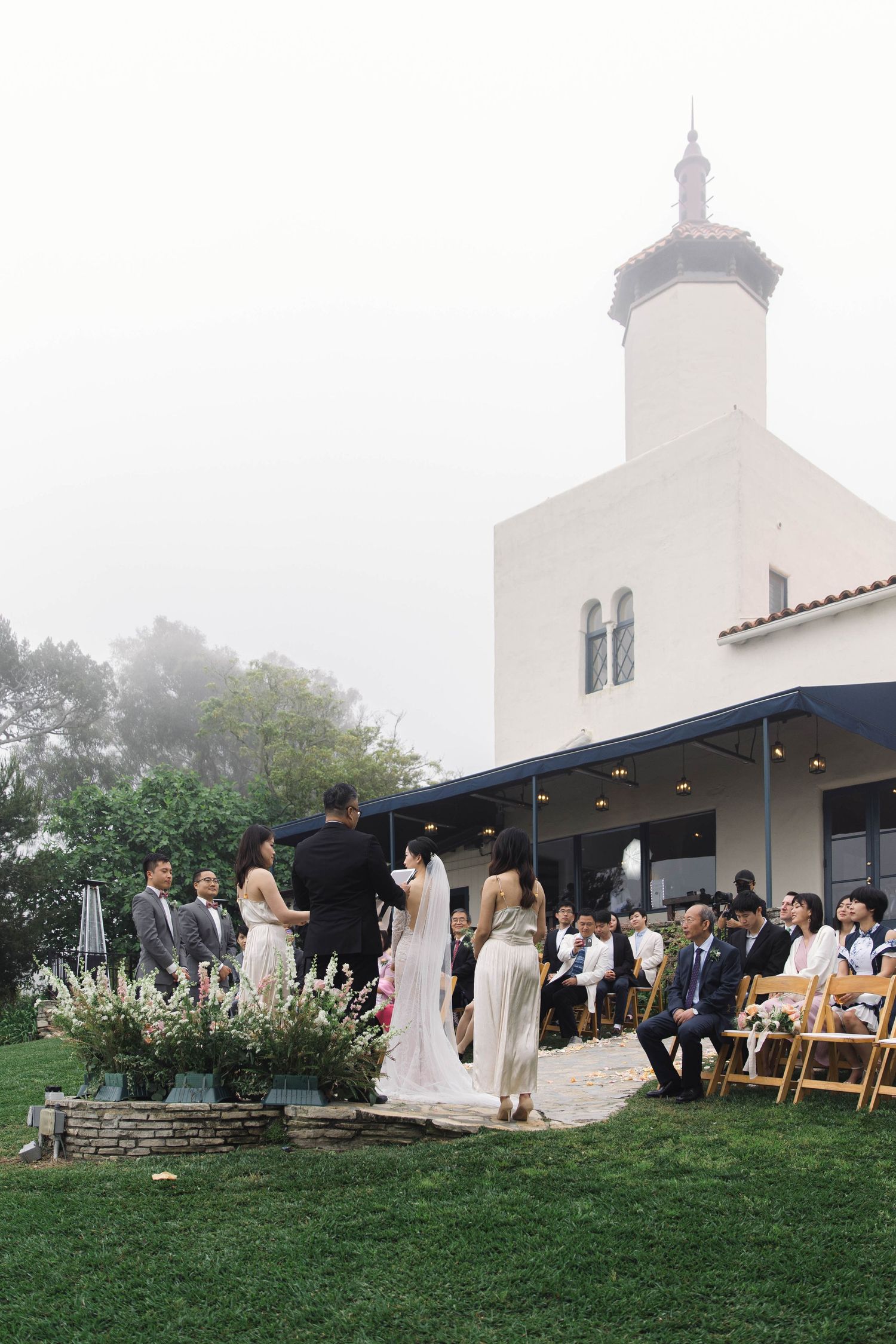 Outdoor wedding ceremony setup with white chairs on grass lawn near a church building.
