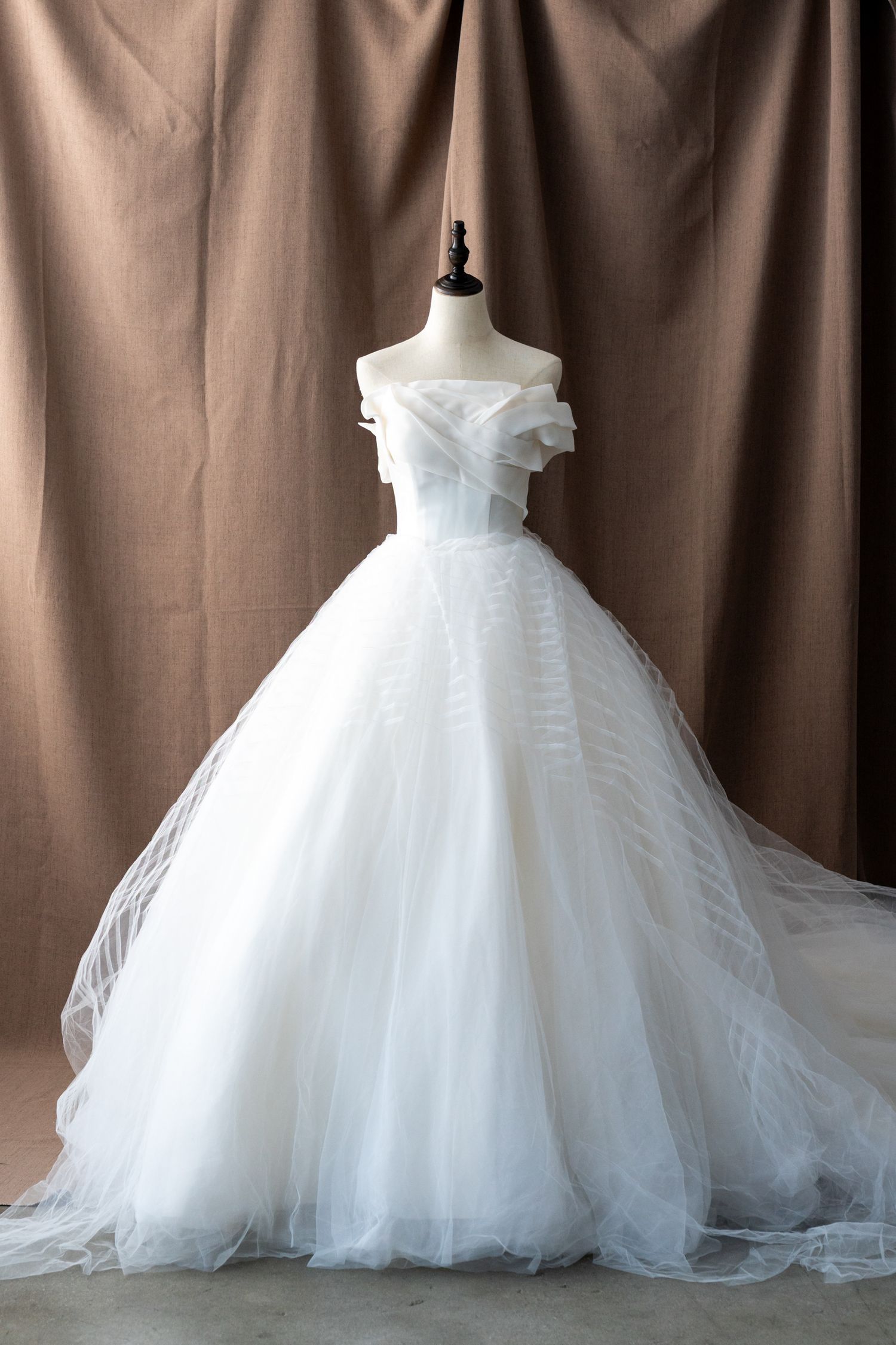 Full-skirted white wedding ball gown with off-shoulder design shown on dress form.
