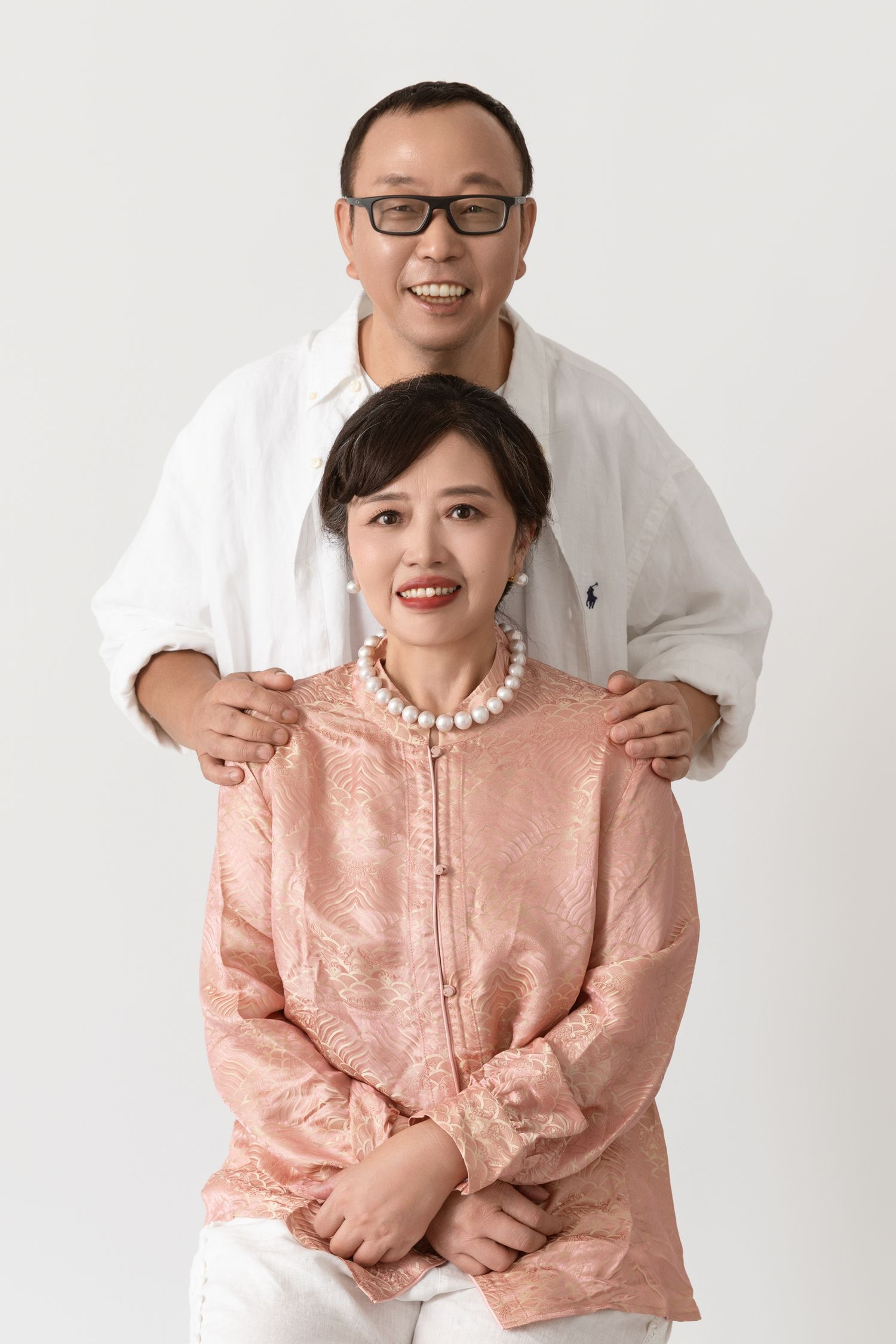 Couple in pink and white outfits pose playfully for studio portraits.