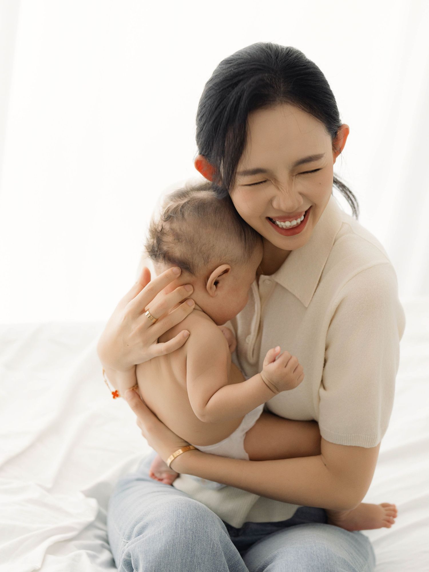 Parent and baby sharing tender moment in bright white studio setting.