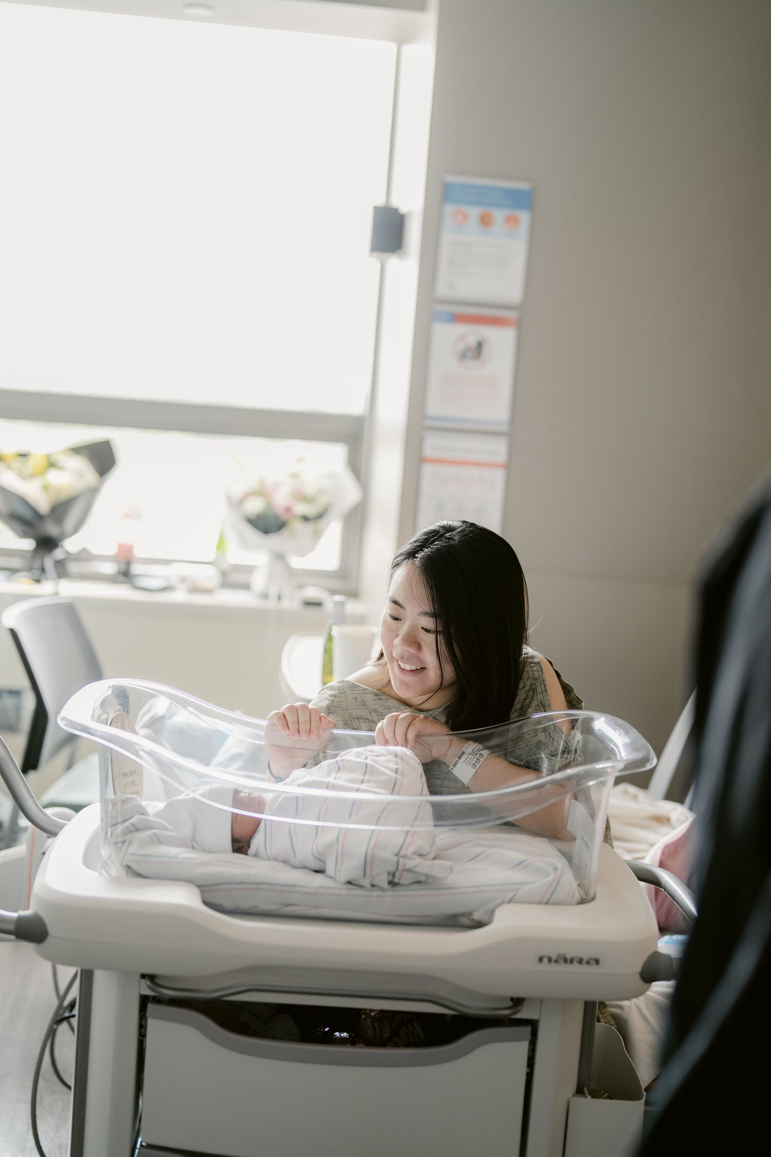 Caregiver leaning over hospital bassinet with newborn inside.