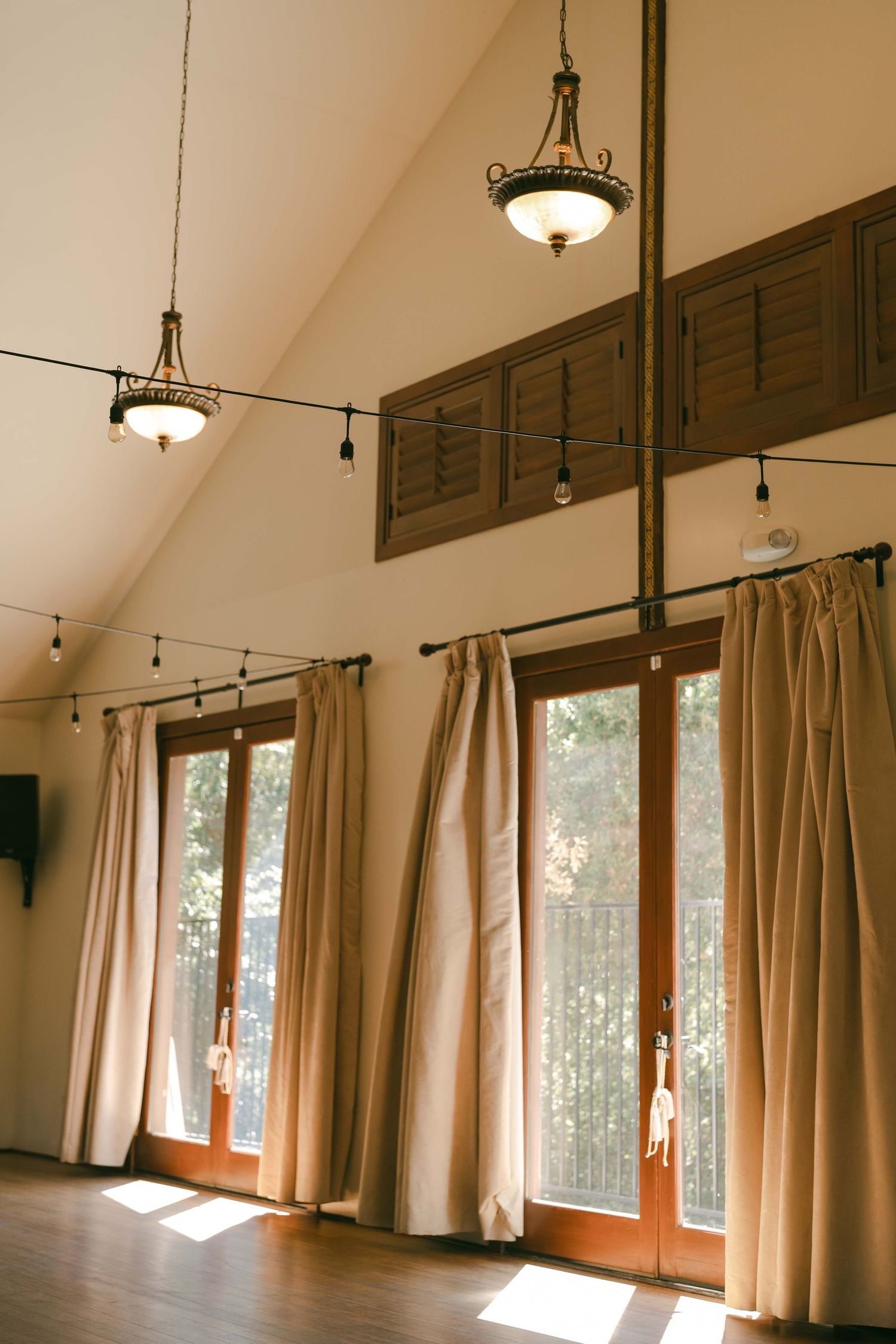 Interior of a room with vaulted ceilings, pendant lights, and beige curtains covering large windows.