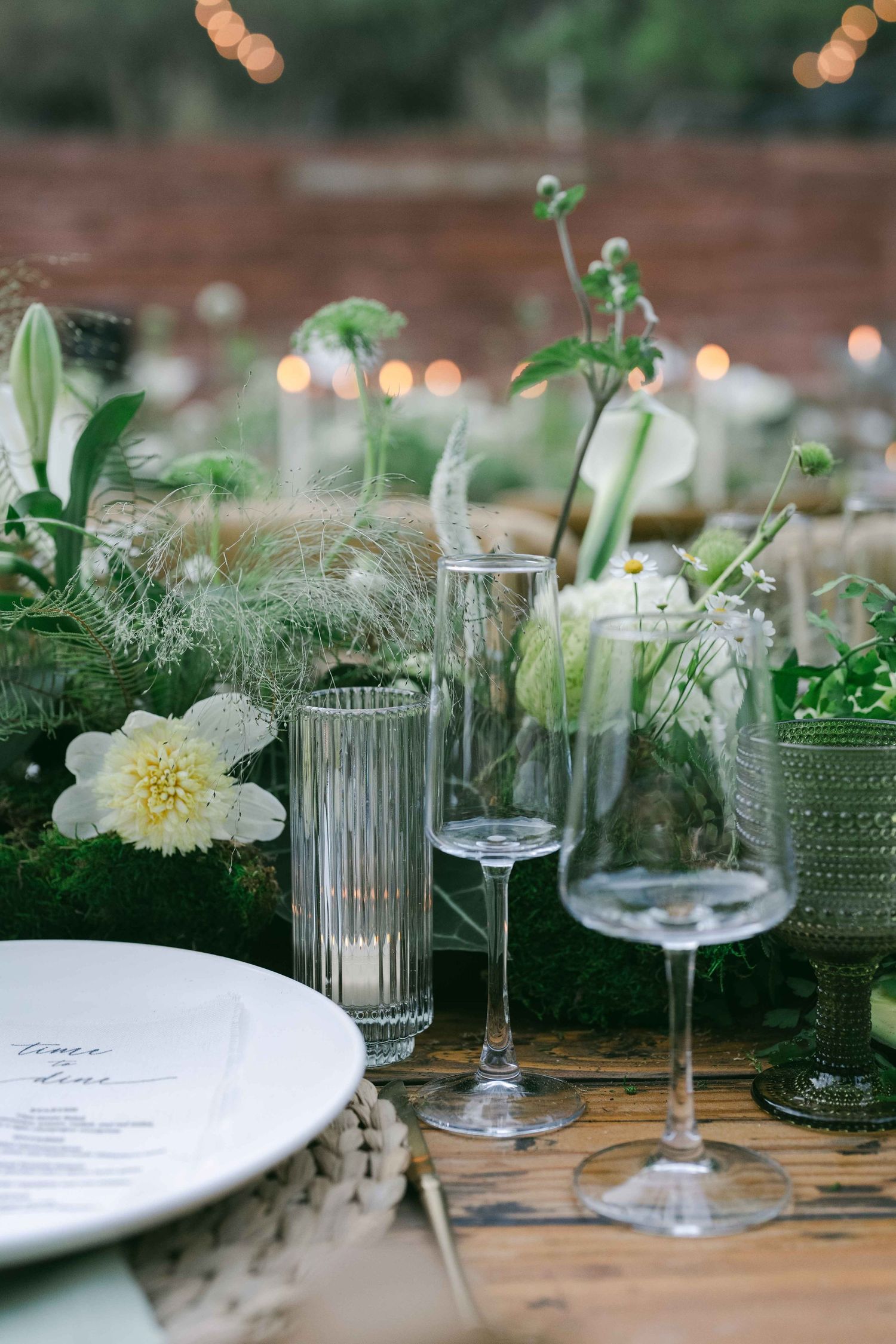 Detailed view of glassware and white floral arrangements on rustic wooden tables.