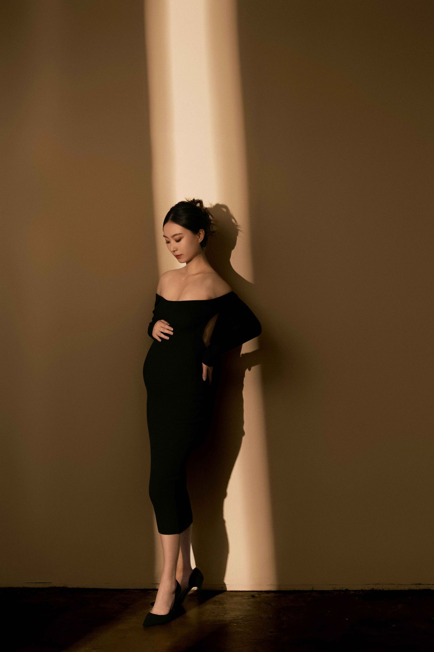 Artistic maternity silhouette of woman in black dress against dramatic lighting.