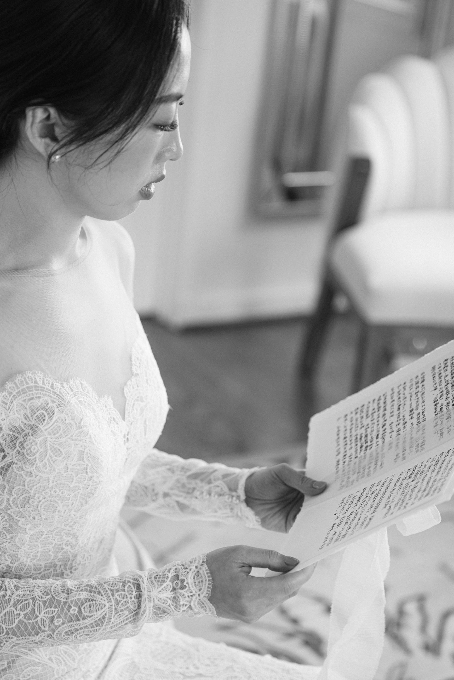 Close-up of a person in white lace reading a letter or document in soft natural light.