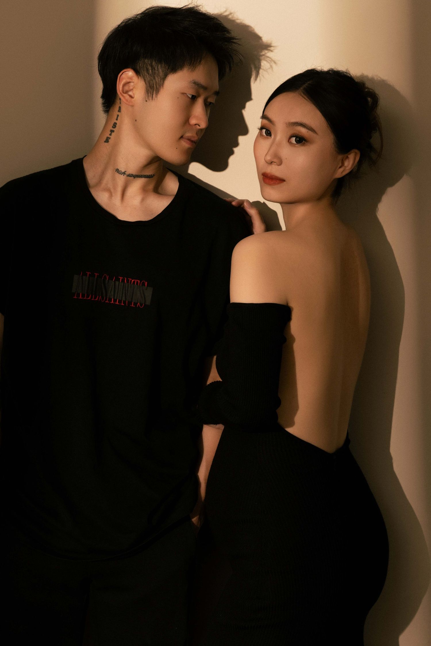 Dramatic portrait of couple in black attire against shadowed beige background.