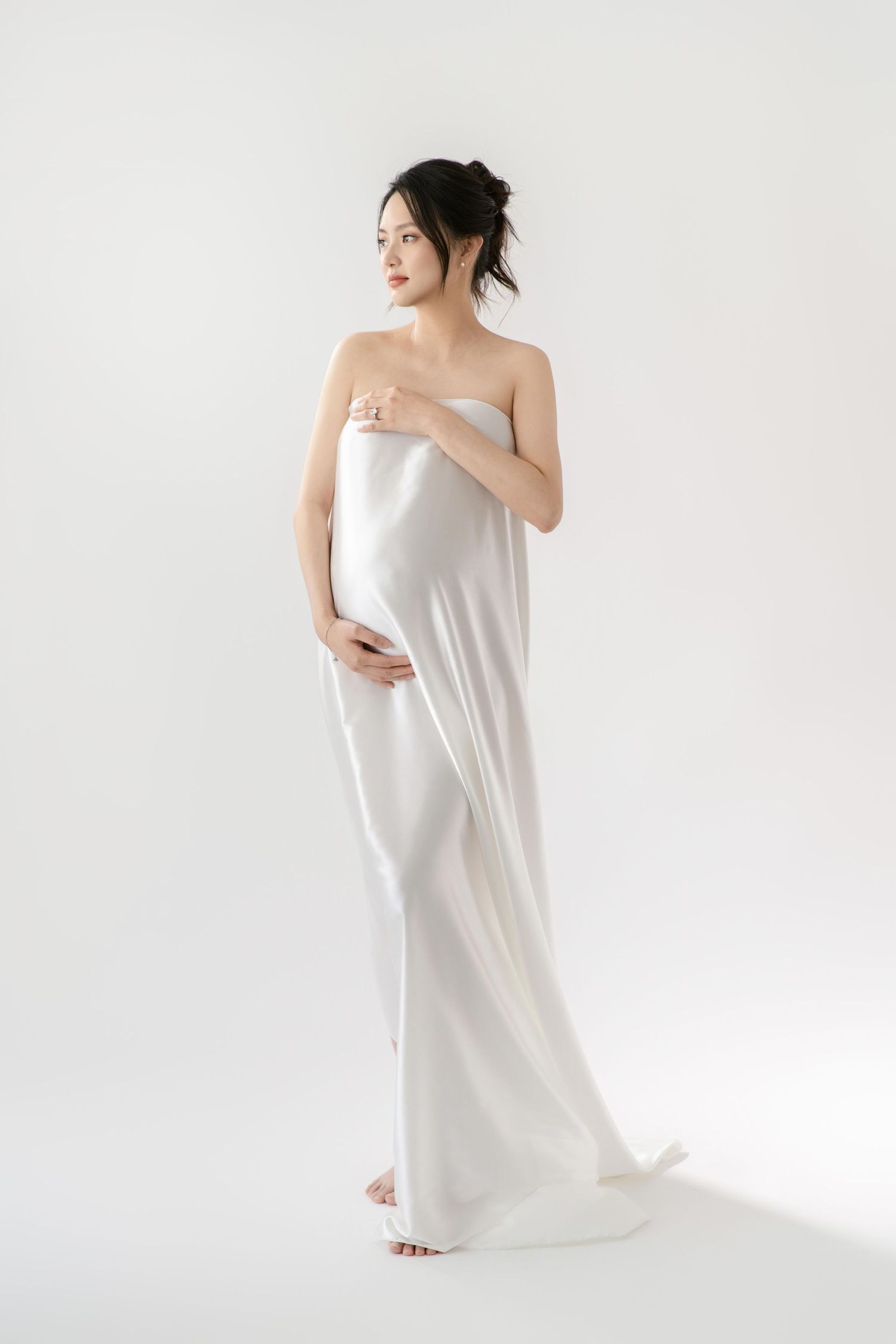 Minimalist maternity portrait with white fabric draping against light background.