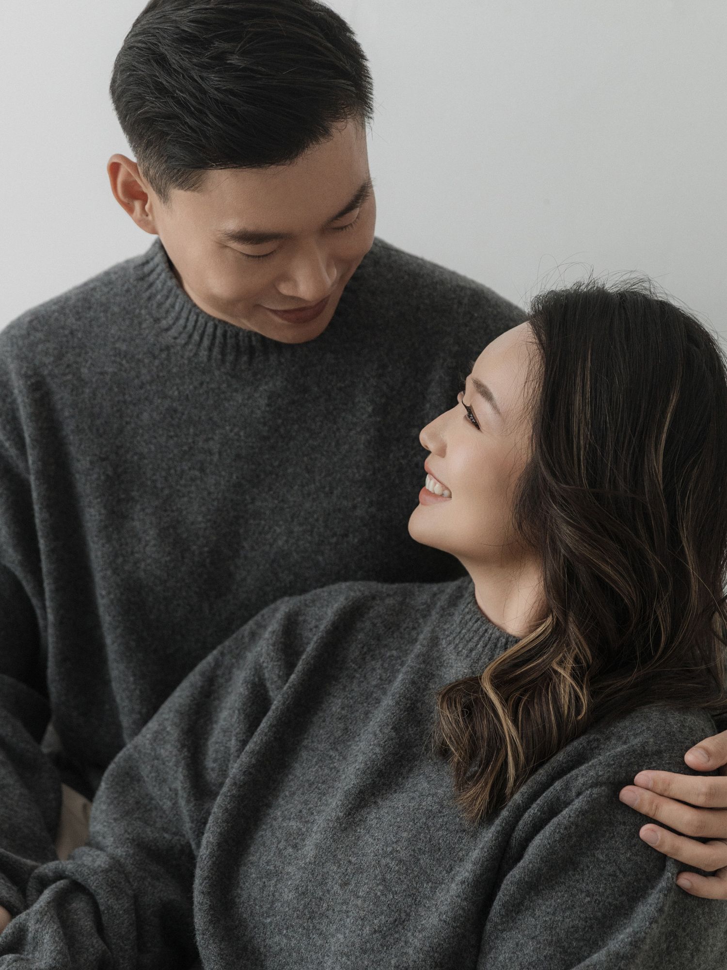 Romantic couple portrait with both in gray sweaters against white backdrop.