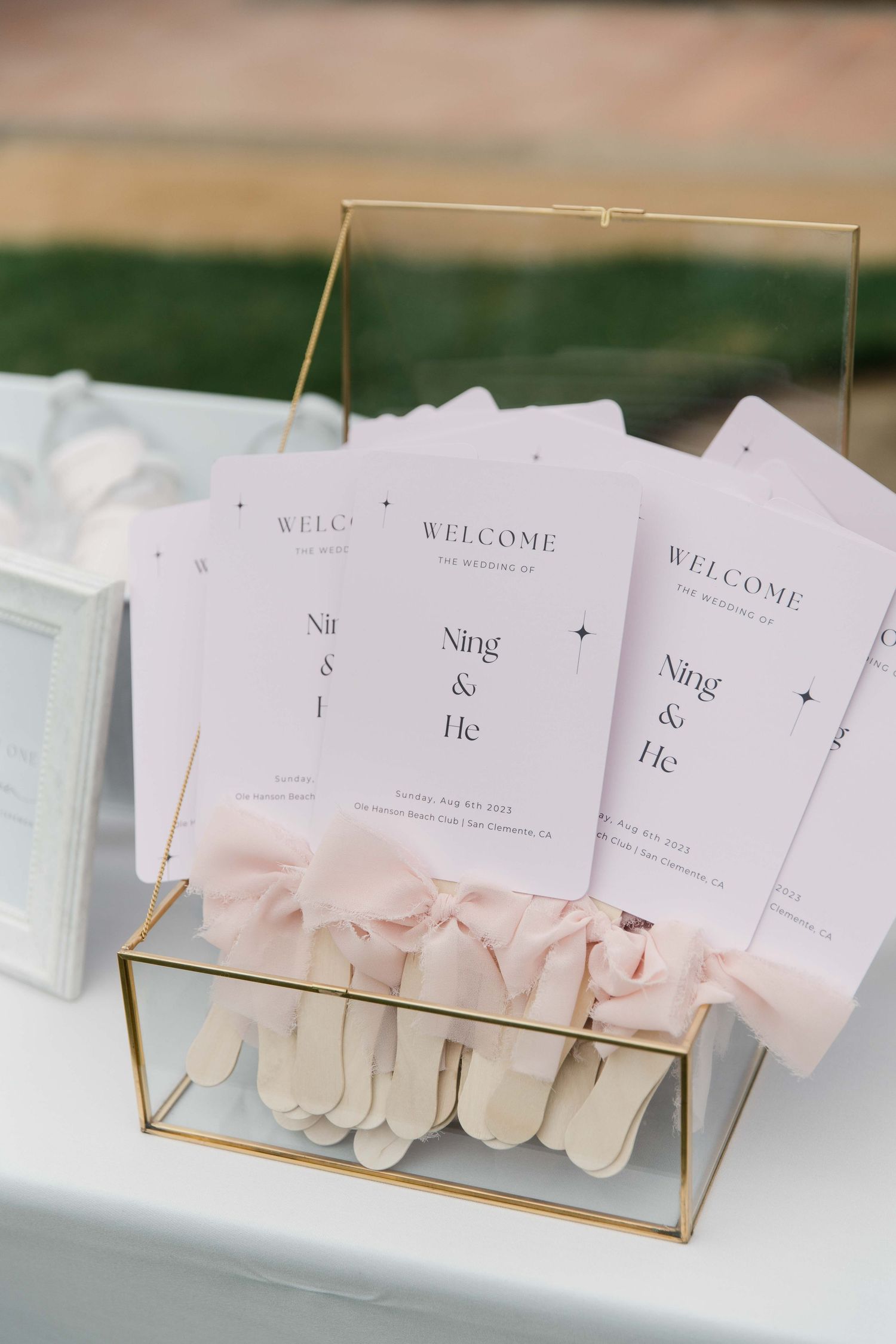 Wedding welcome cards with pink bows displayed in gold geometric holders.
