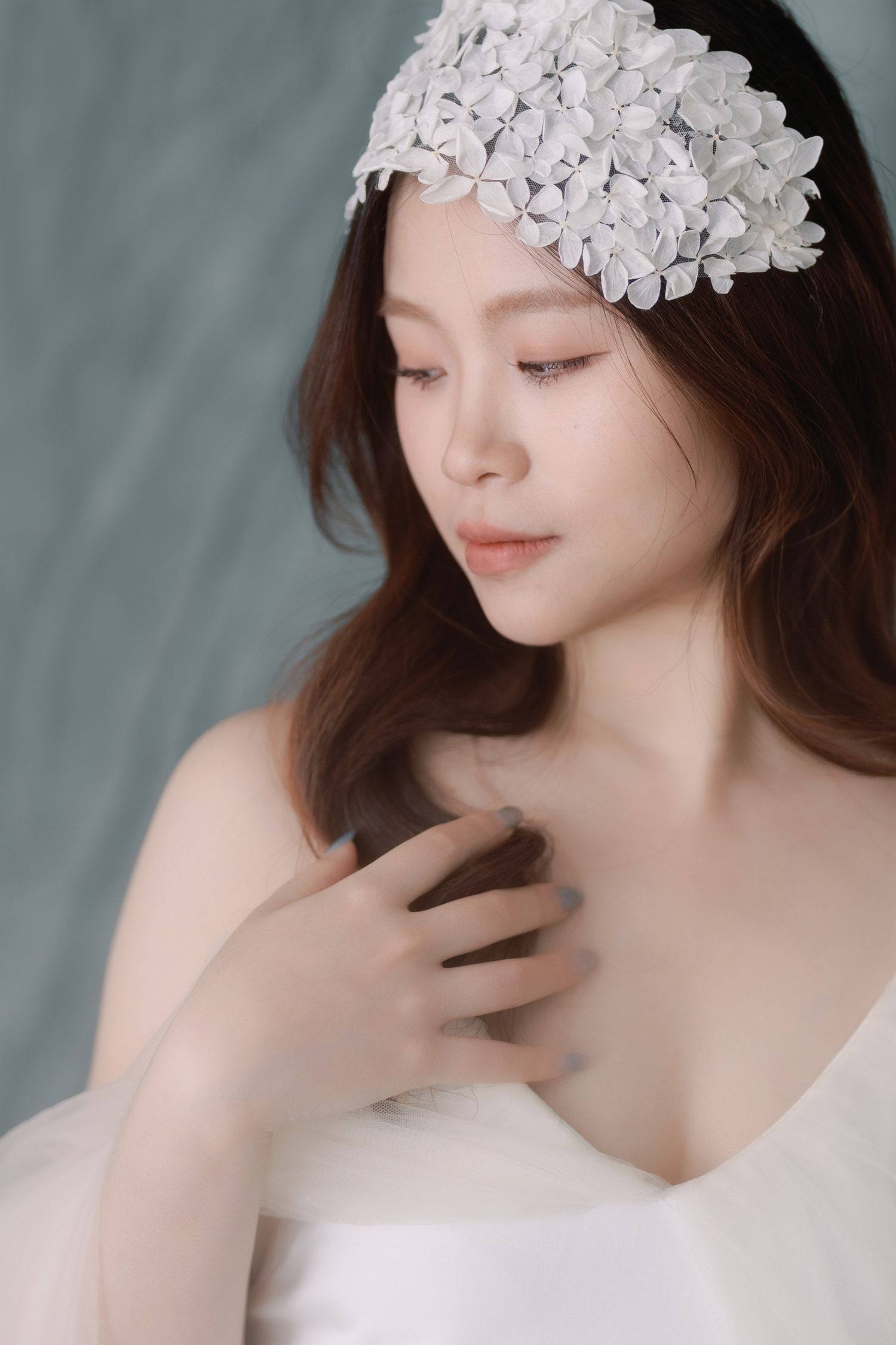 Elegant portrait with delicate white floral headpiece against blue-grey background.