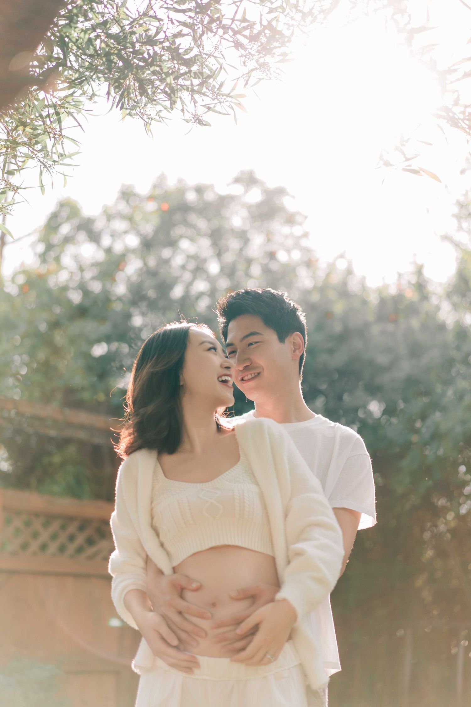 Romantic outdoor maternity session with couple in white clothing during golden hour.