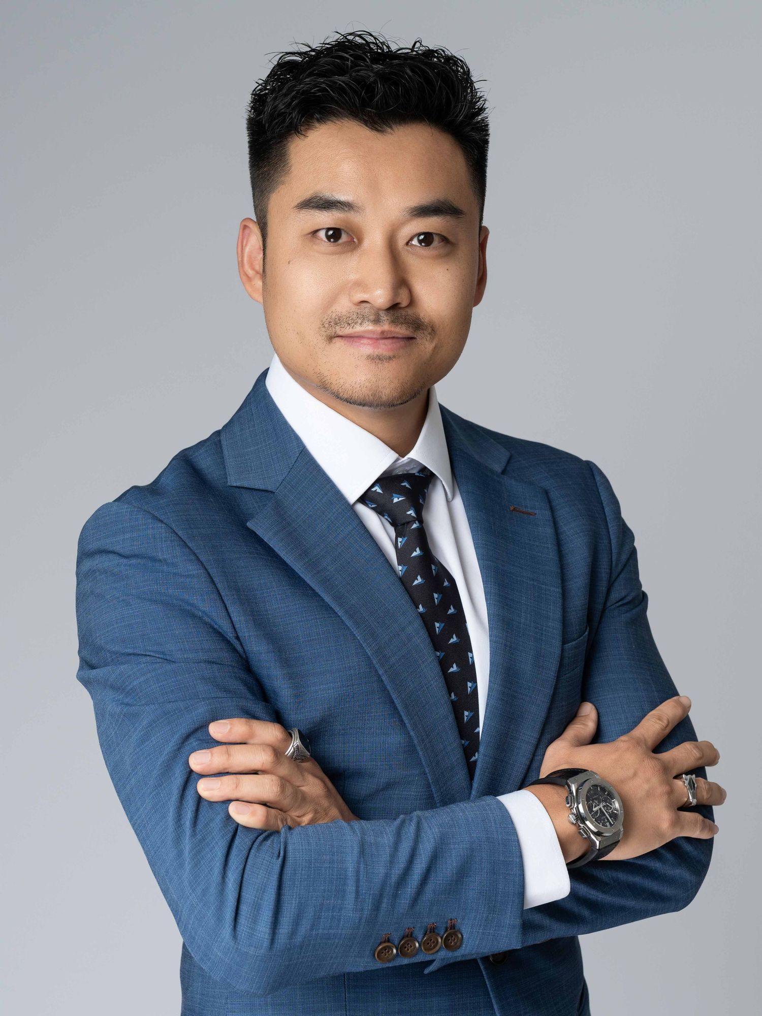 Professional headshots of businessman in navy suit against grey background.