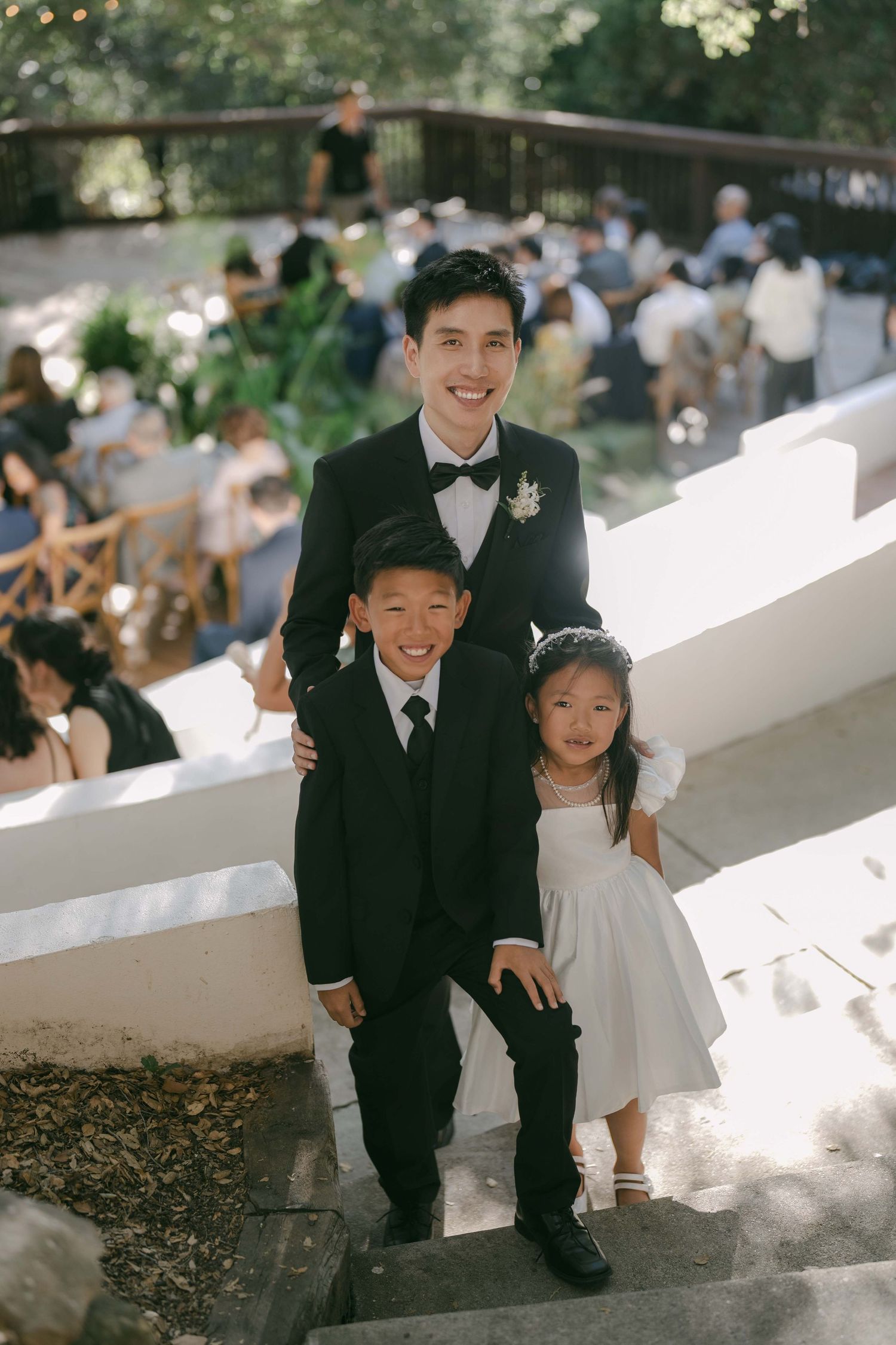 Wedding guests seated on white steps during outdoor ceremony.
