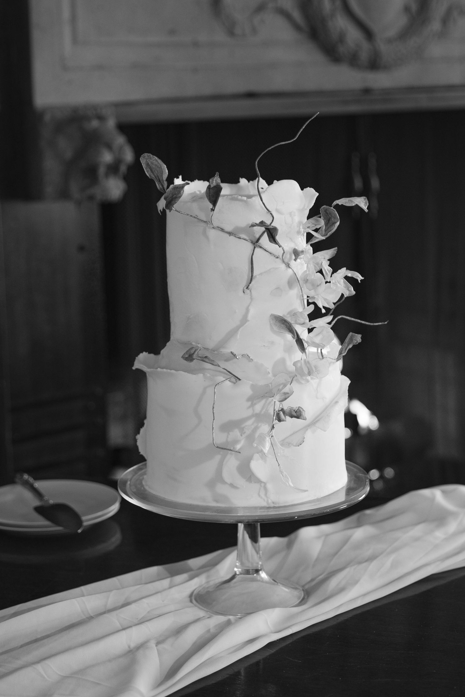 Black and white photo of a two-tier white wedding cake decorated with delicate floral elements.