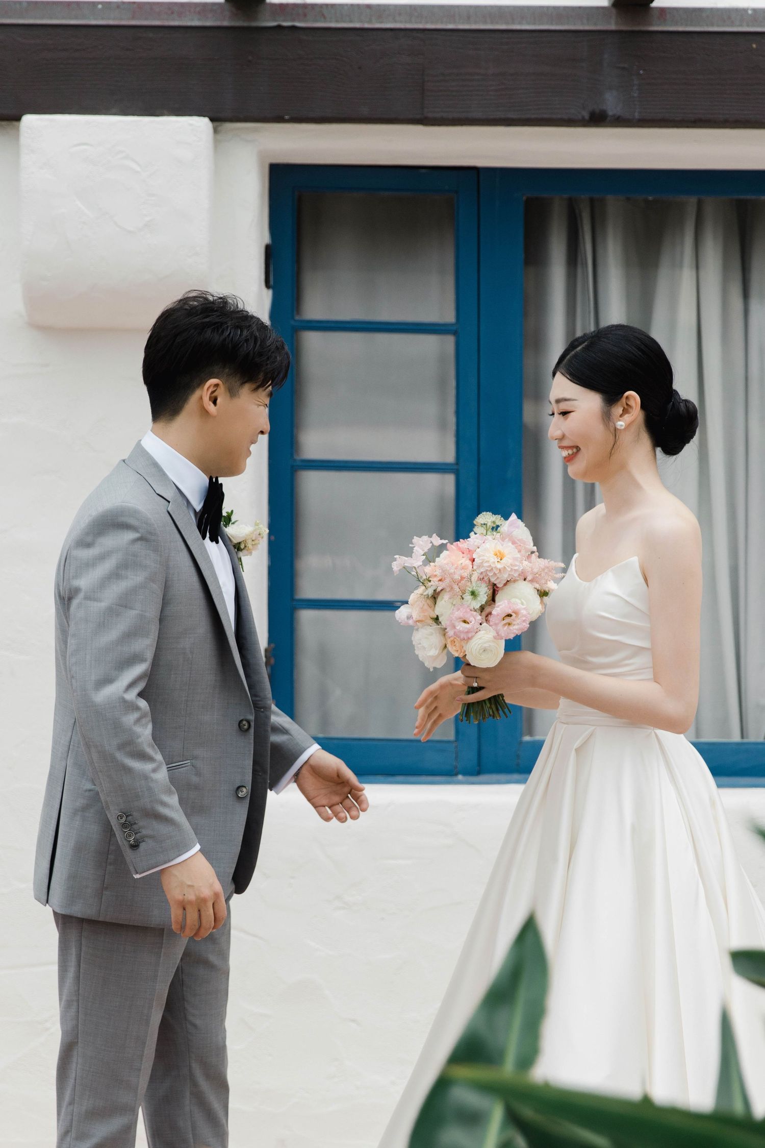 Wedding couple in white dress and gray suit sharing a moment outside a building with blue trim.