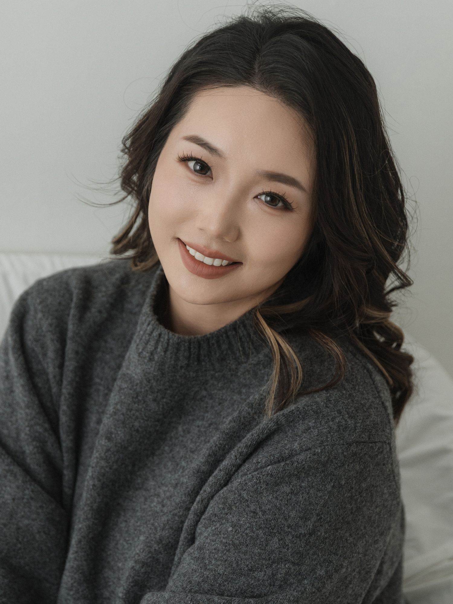 Person in cozy gray sweater poses playfully on light background.