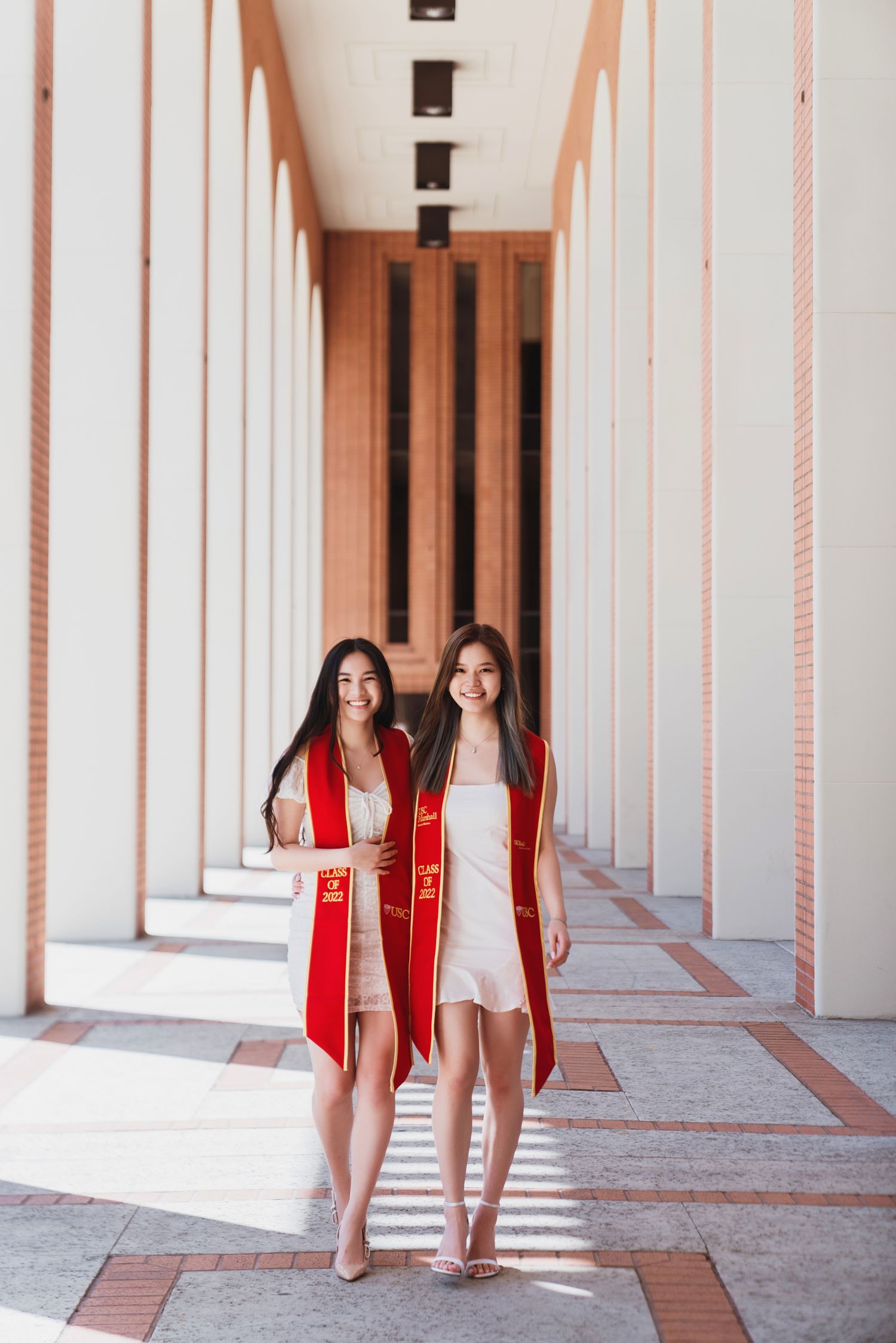 Friends in graduation stoles walking through USC campus colonnade.