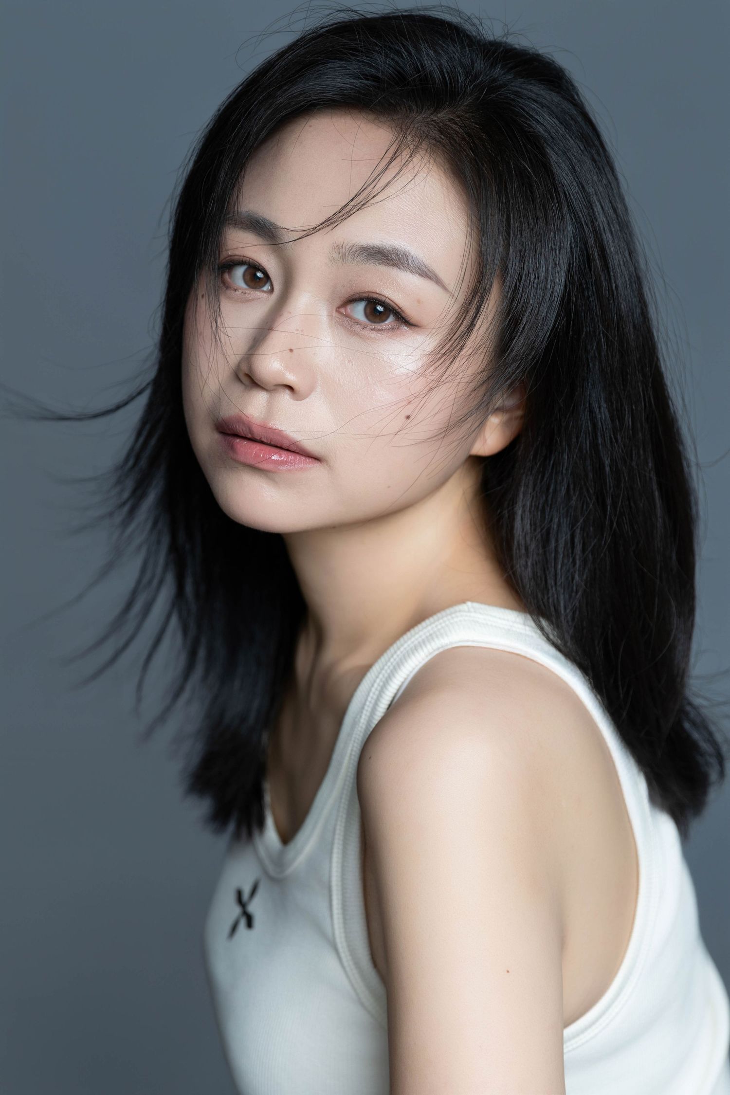 Studio portrait with black hair and white tank top against grey background.