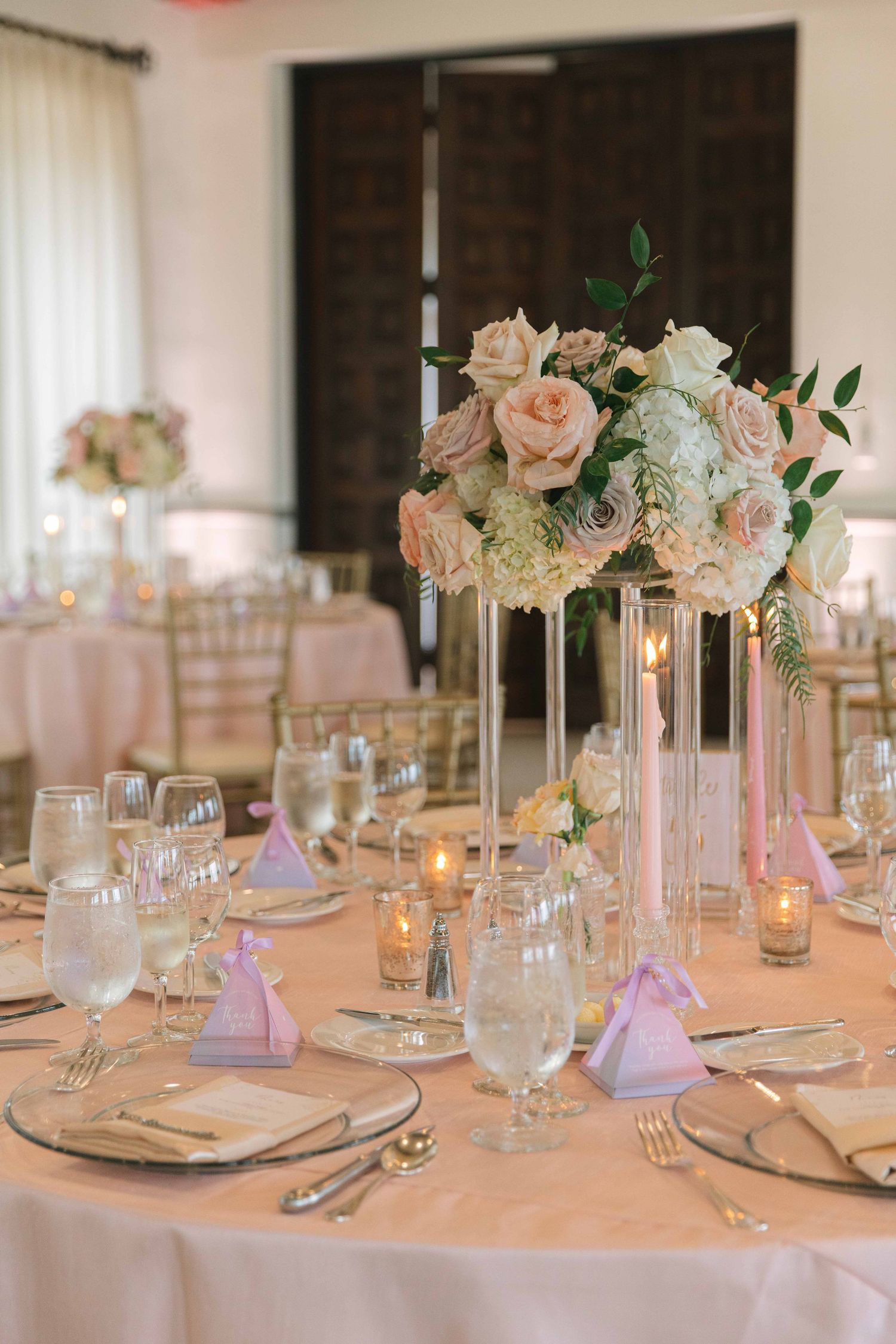 Wedding table setting with tall pink and white floral centerpiece, candles, and purple napkin accents.