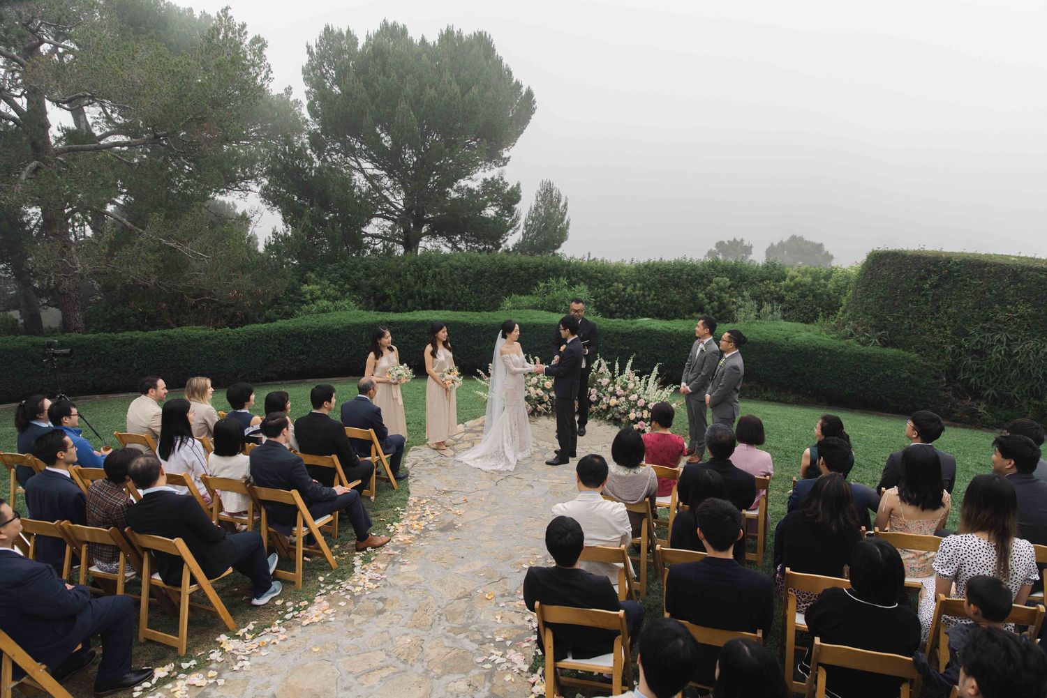 Guests seated in wooden chairs watch an outdoor wedding ceremony with mountain views.