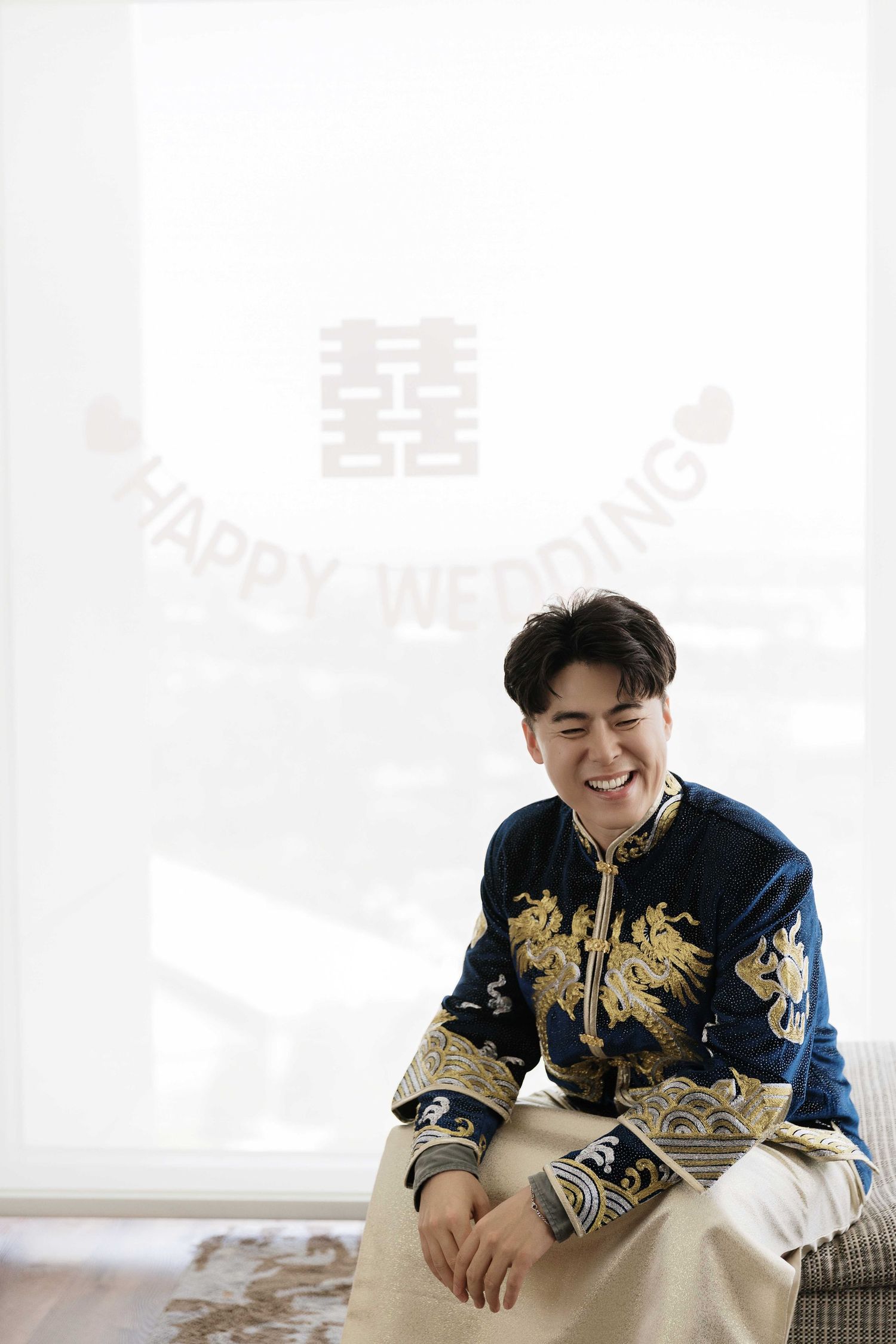 Person wearing traditional navy blue Chinese wedding attire with gold embroidery smiles while seated.