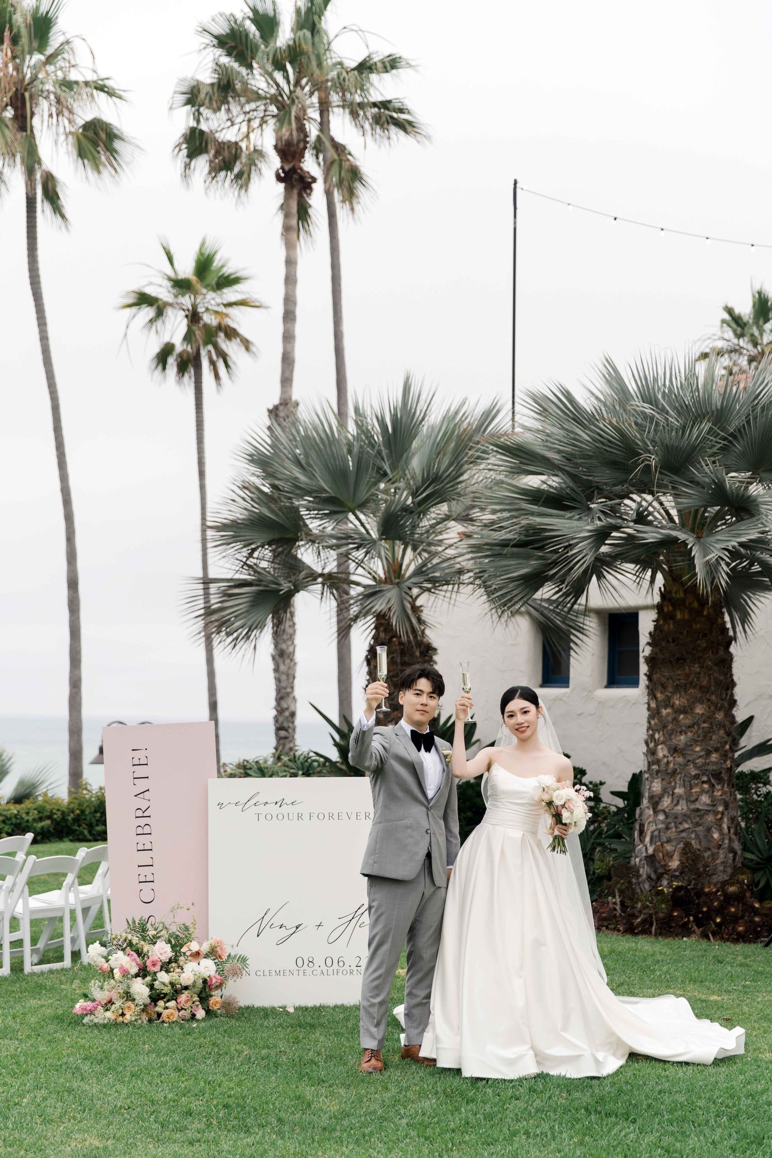 Couple poses for portrait by elegant wedding signage with palm trees in background.