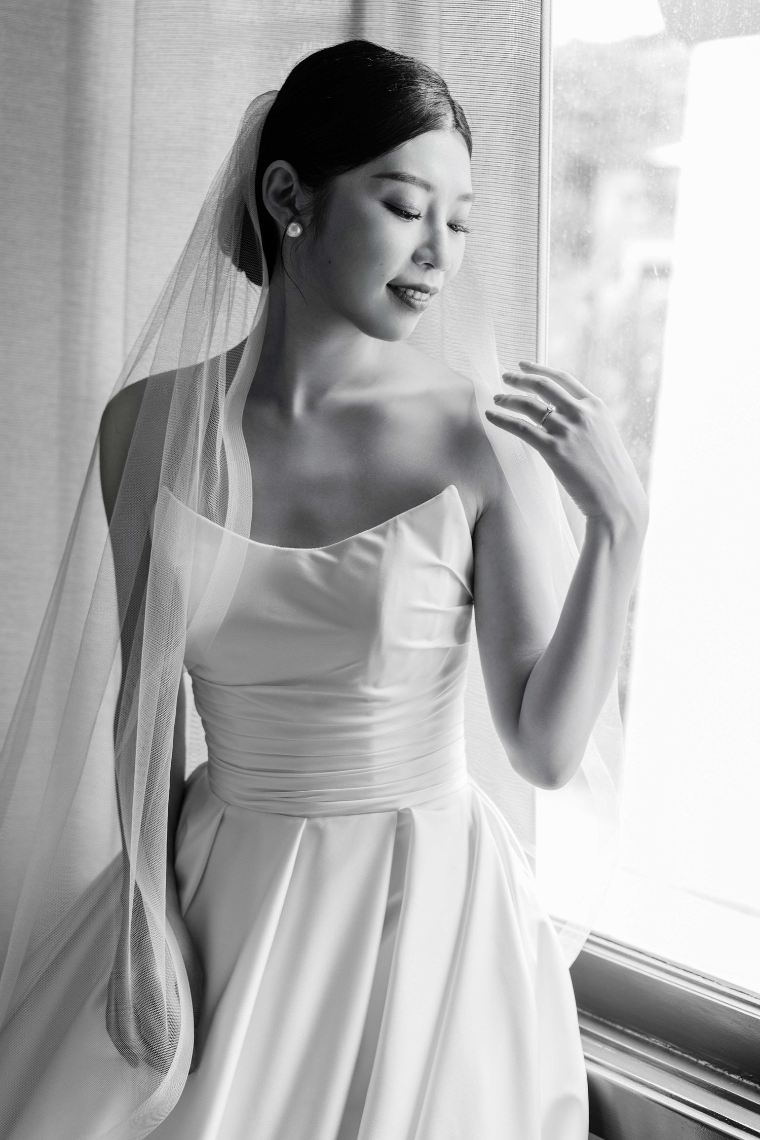 Elegant bridal portraits in black and white showing a flowing wedding dress and veil near a window.