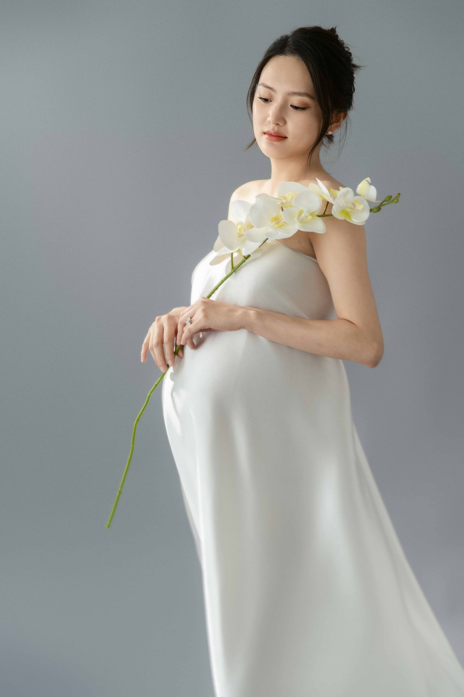 Artistic portrait series with white orchid stem and flowing fabric in grey studio.