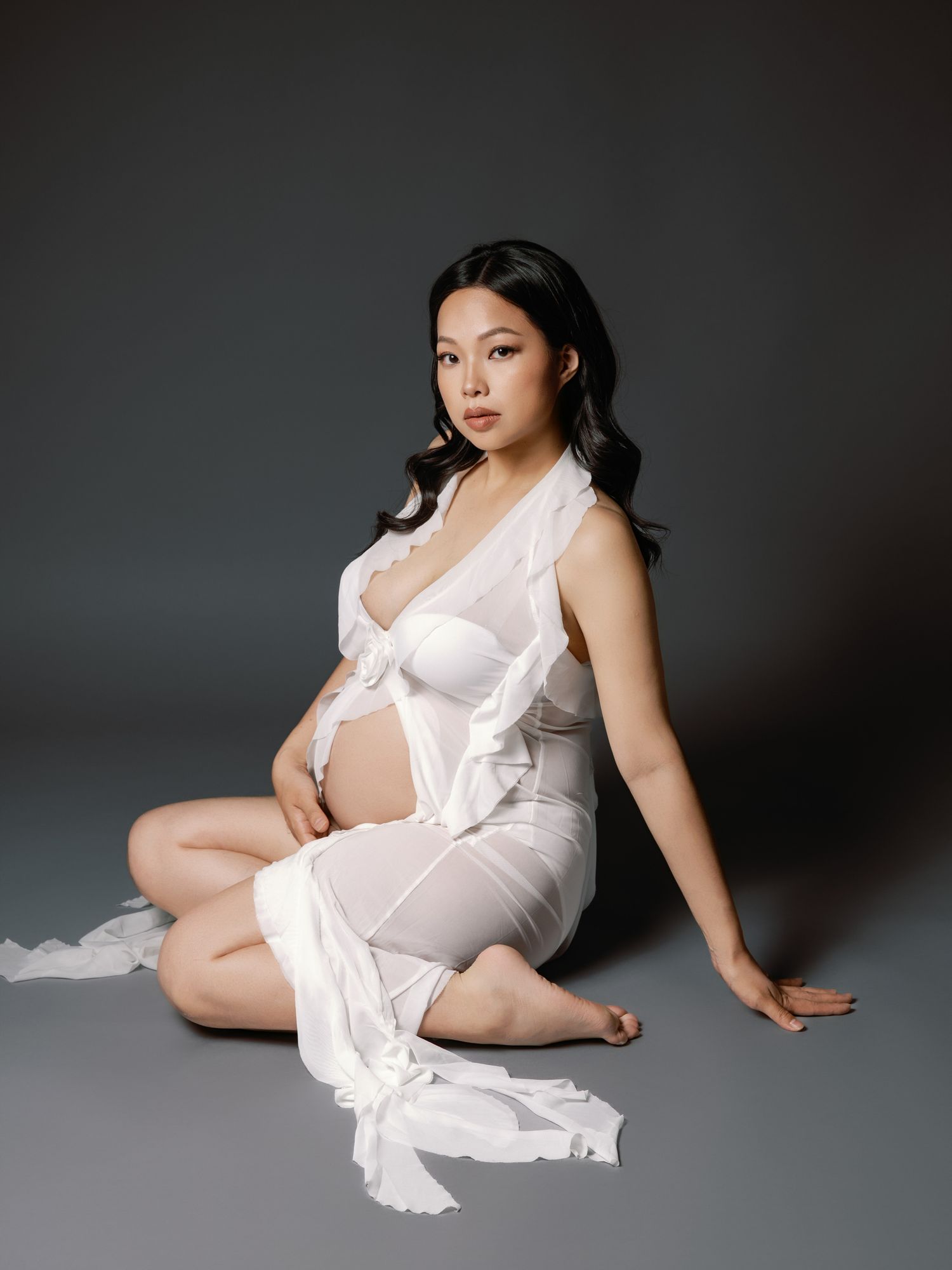 Artistic maternity portraits in white dress against dark background.