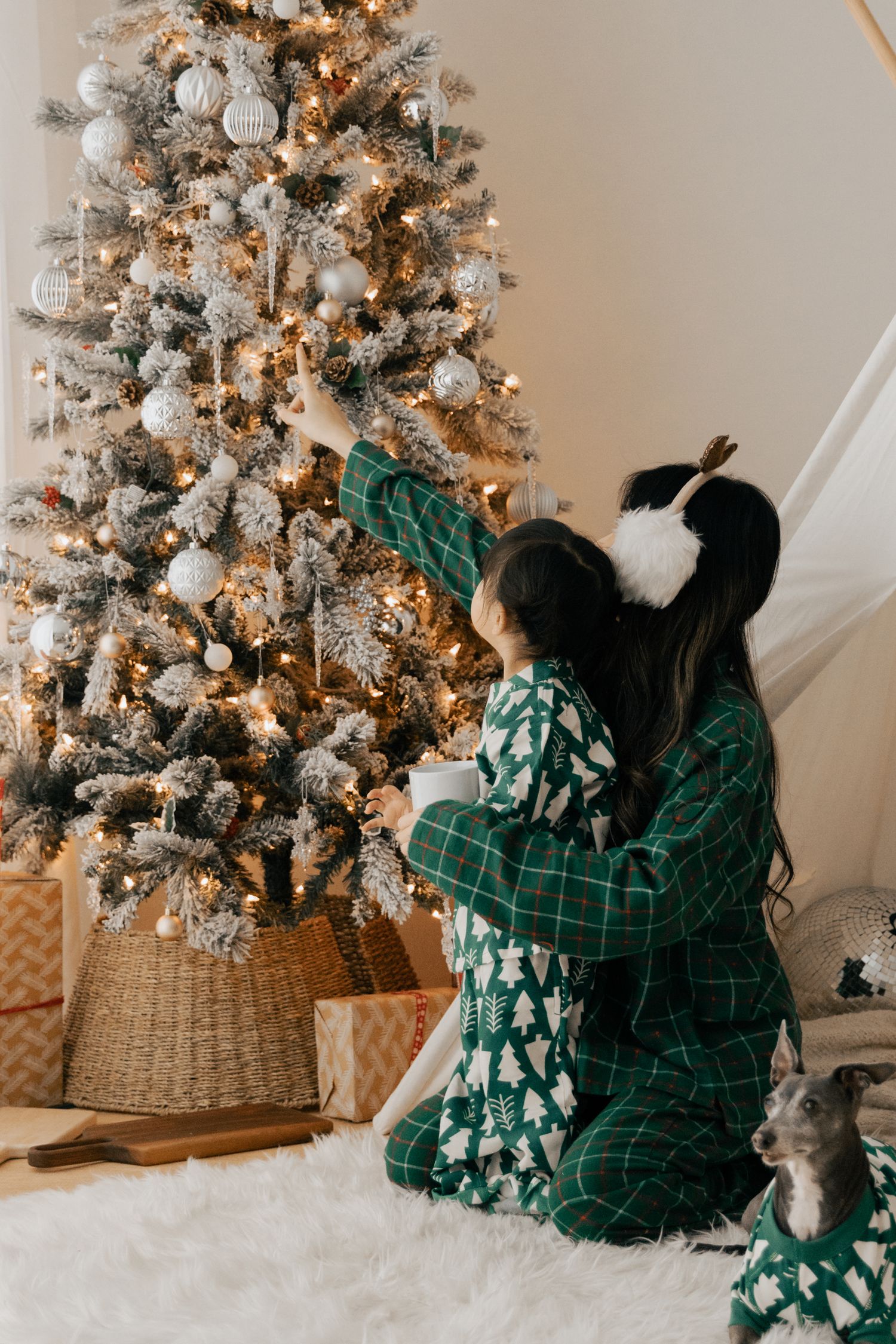 Family members decorating a flocked Christmas tree with silver and white ornaments.