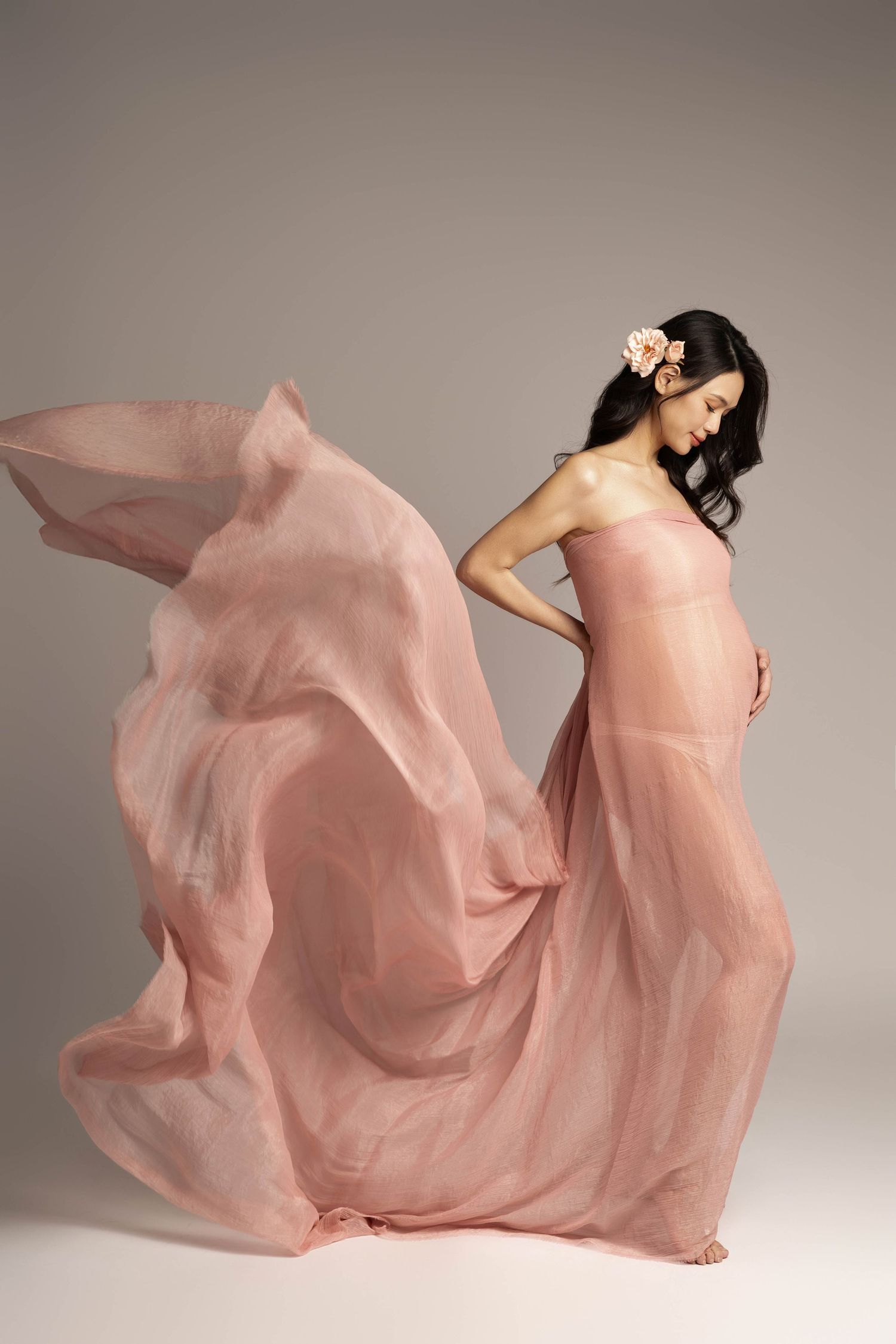Flowing pink fabric creates dramatic movement in artistic maternity photography.