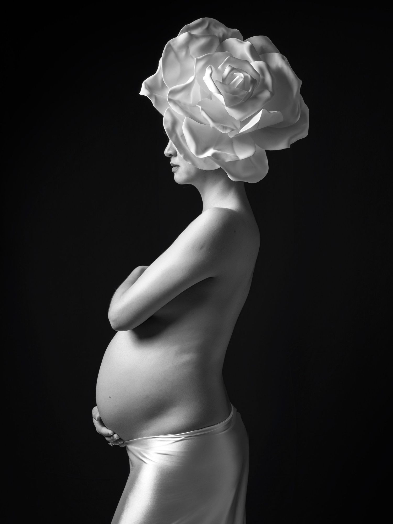 Surreal black and white portrait with rose-shaped headdress and pregnant silhouette.