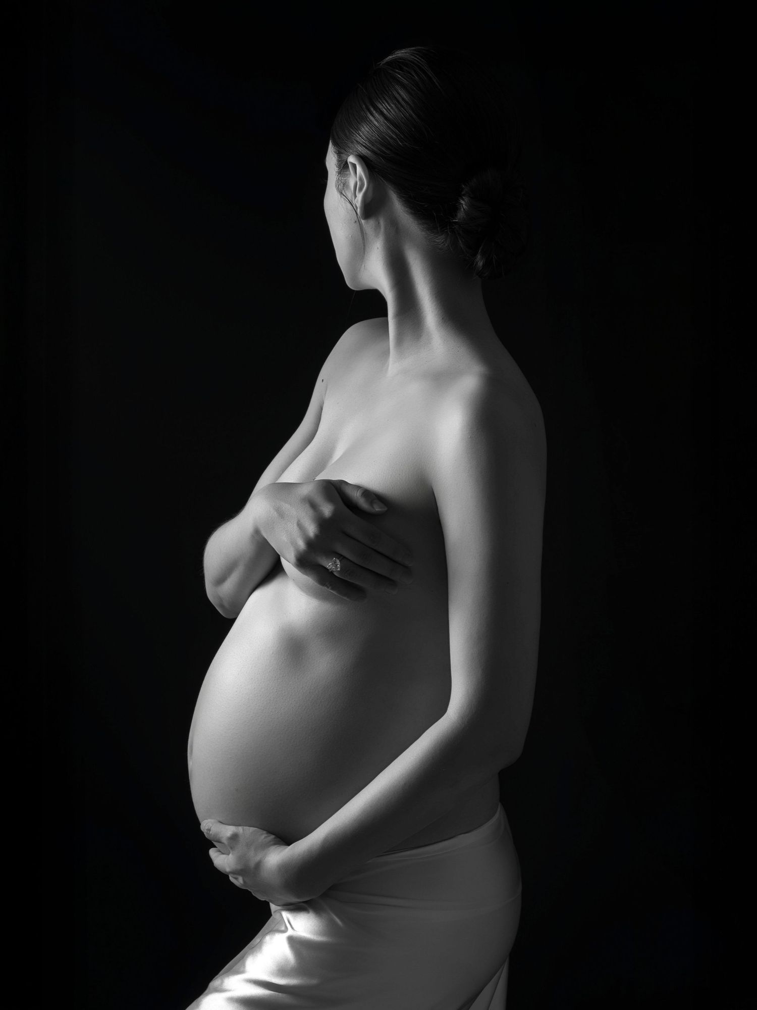 Dramatic black and white side view of expectant mother in studio setting.