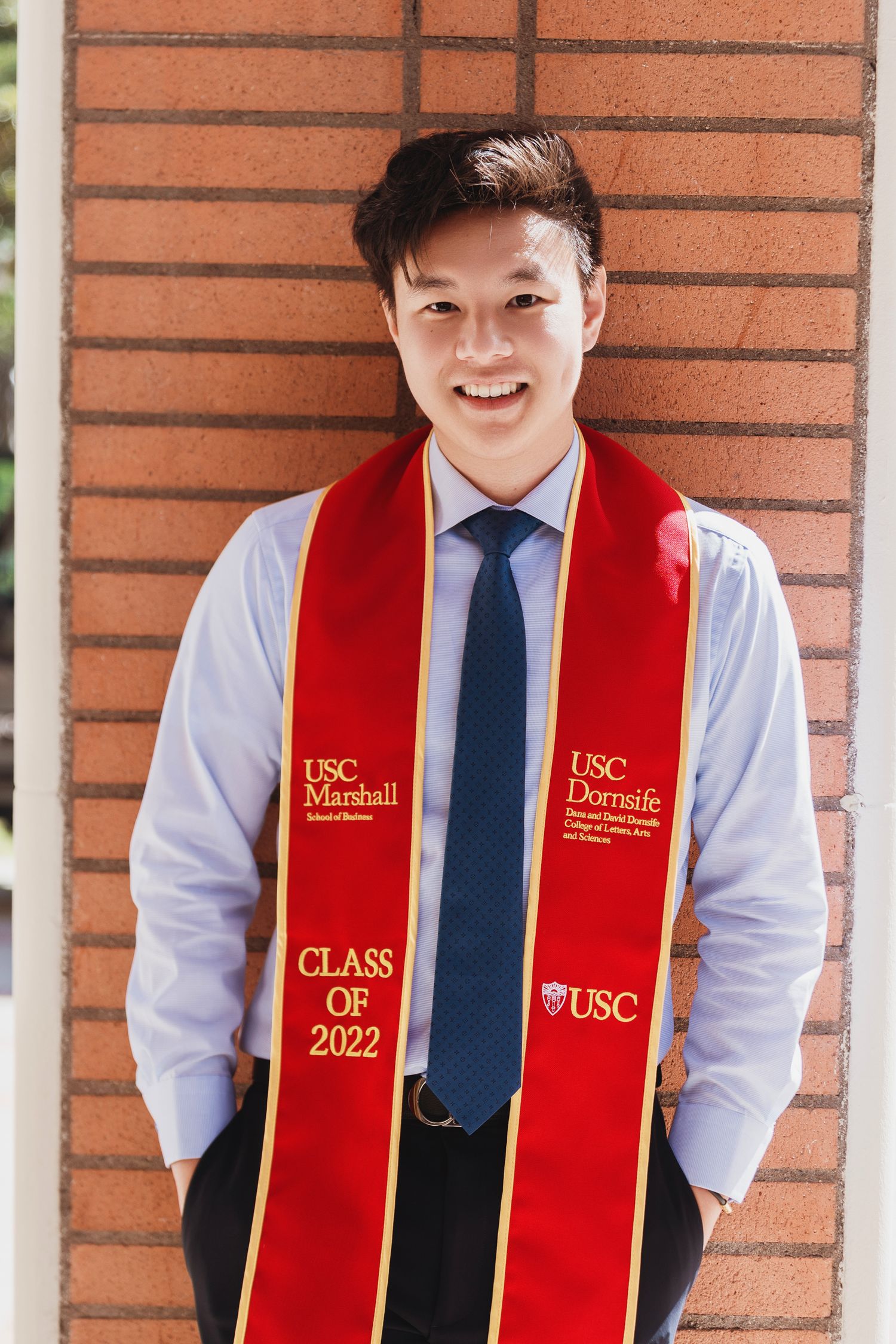 Graduate in dress shirt and tie wearing USC graduation stole smiles at camera.