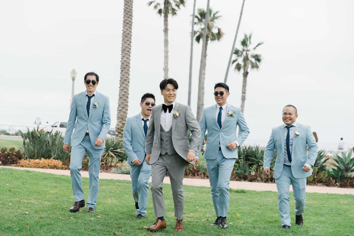 Groomsmen in light blue suits walking across grass during outdoor wedding.