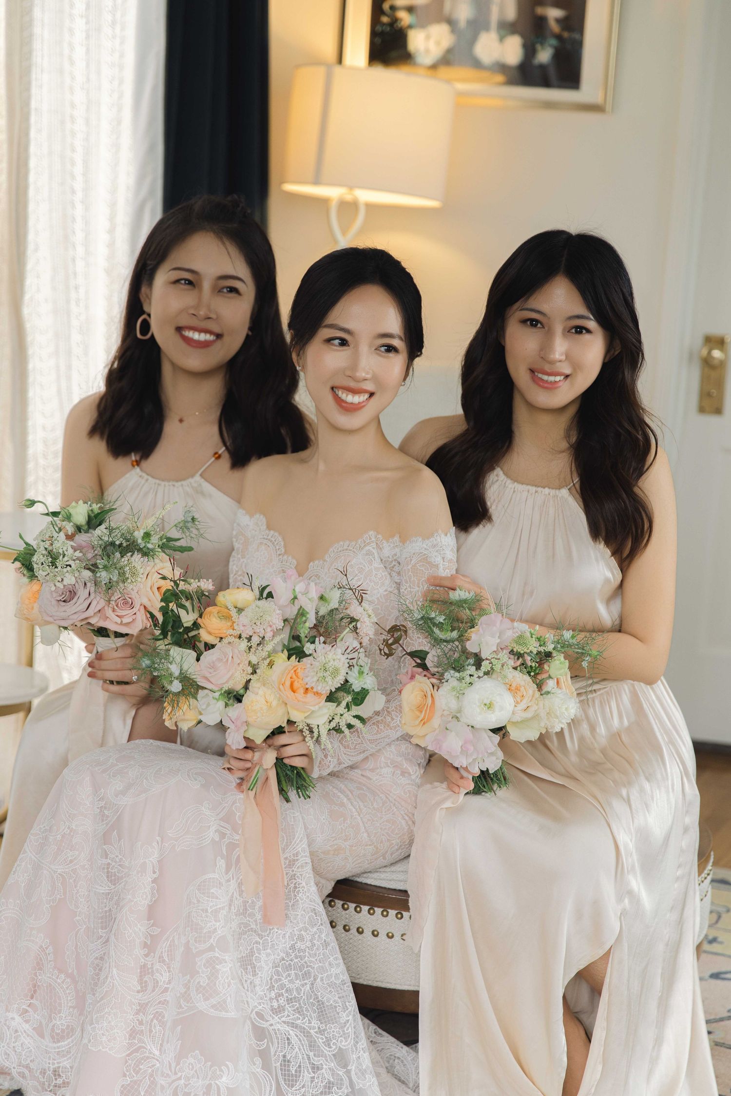 Bridal party holding matching pastel bouquets pose together in flowing white dresses.