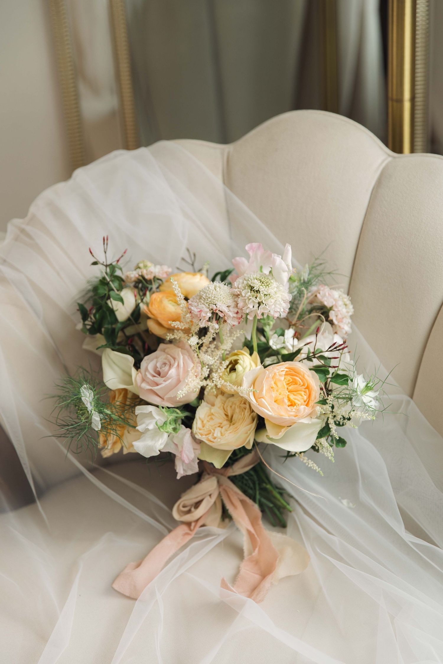 Delicate peach and white floral arrangement with roses and greenery adorns a light tulle backdrop.