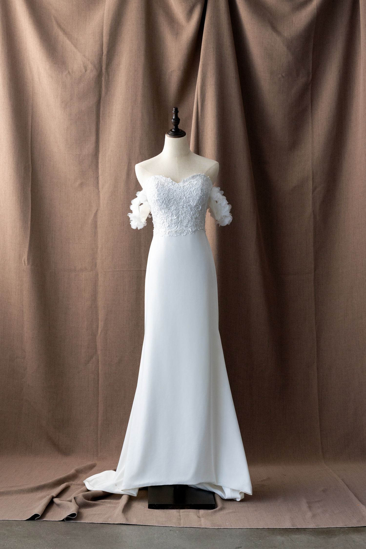 Full-length white wedding dress with lace bodice displayed on mannequin against brown background.
