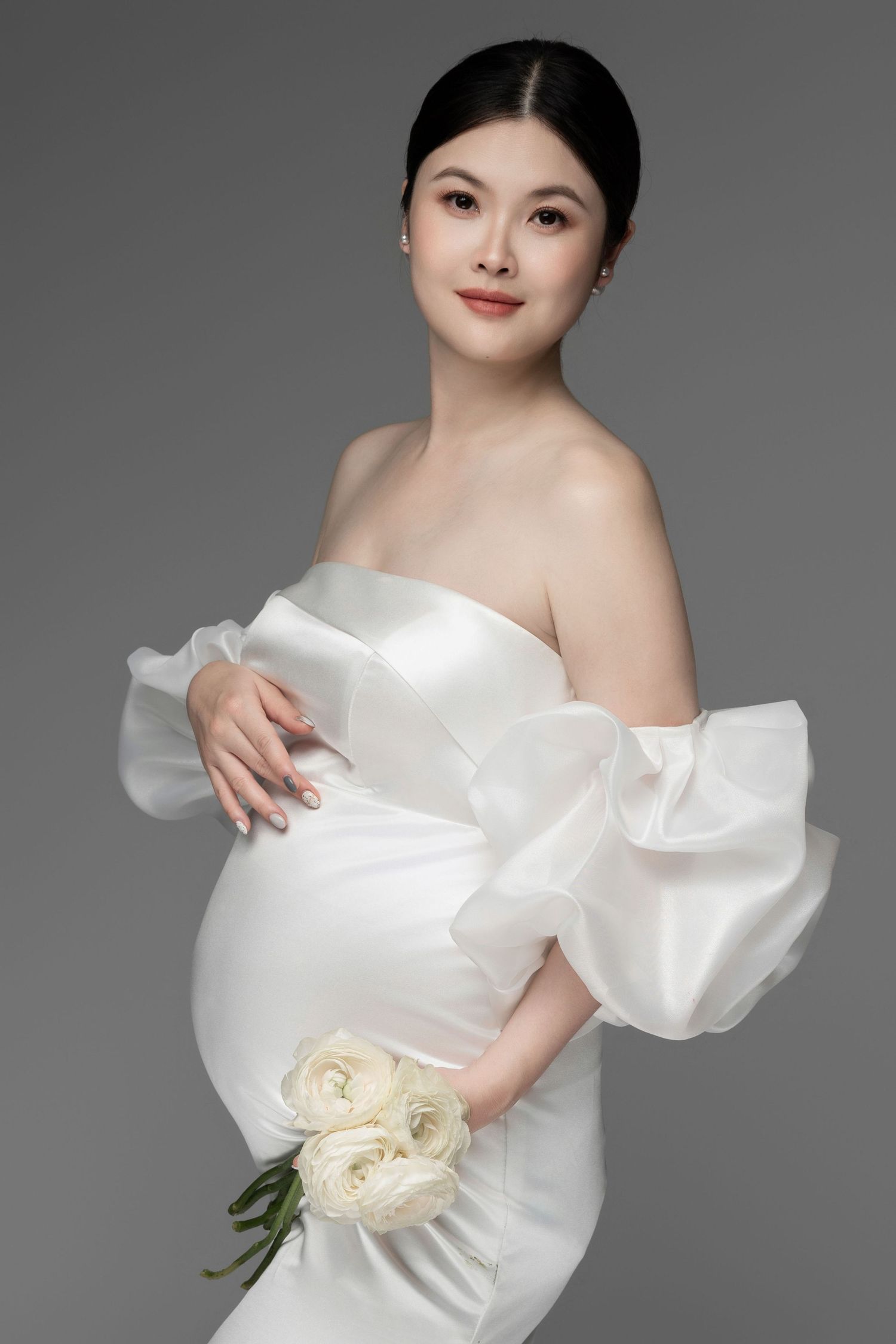 Elegant maternity photos featuring white ruffled dress and cream roses.