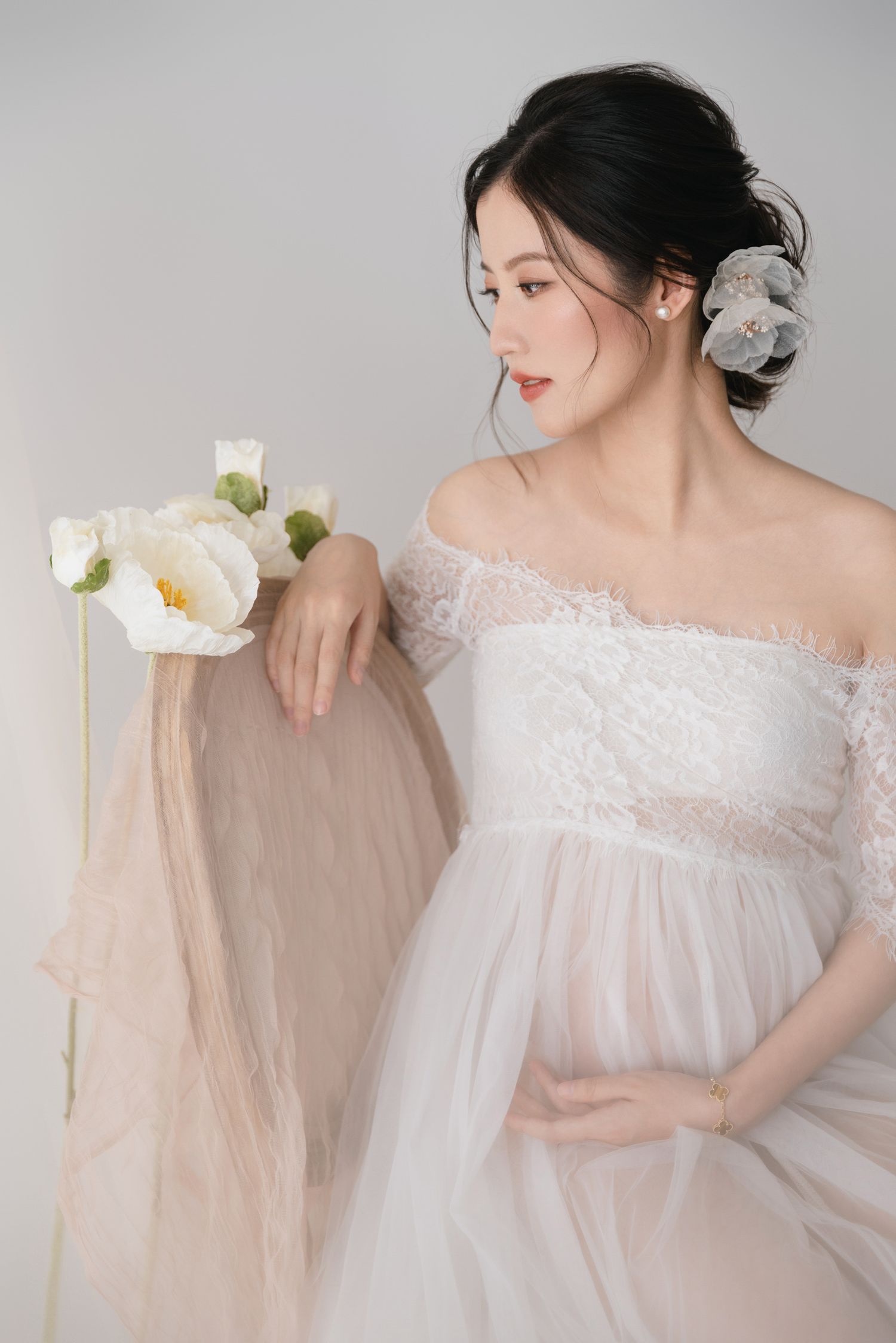Ethereal maternity photoshoot featuring flowing white lace dress against light background.