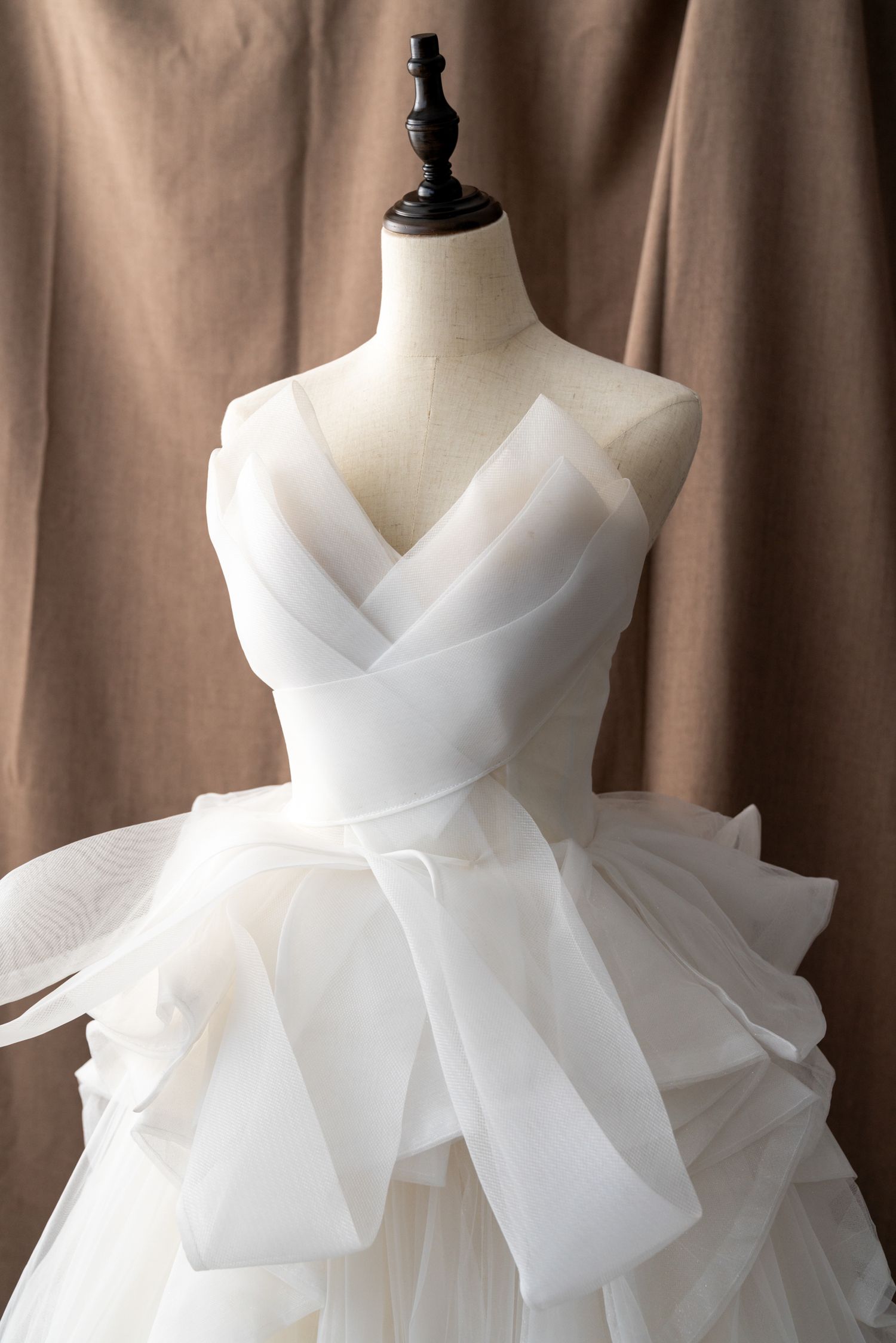 Elegant white bridal gown with layered tulle skirt and bow detail shown on dress form.