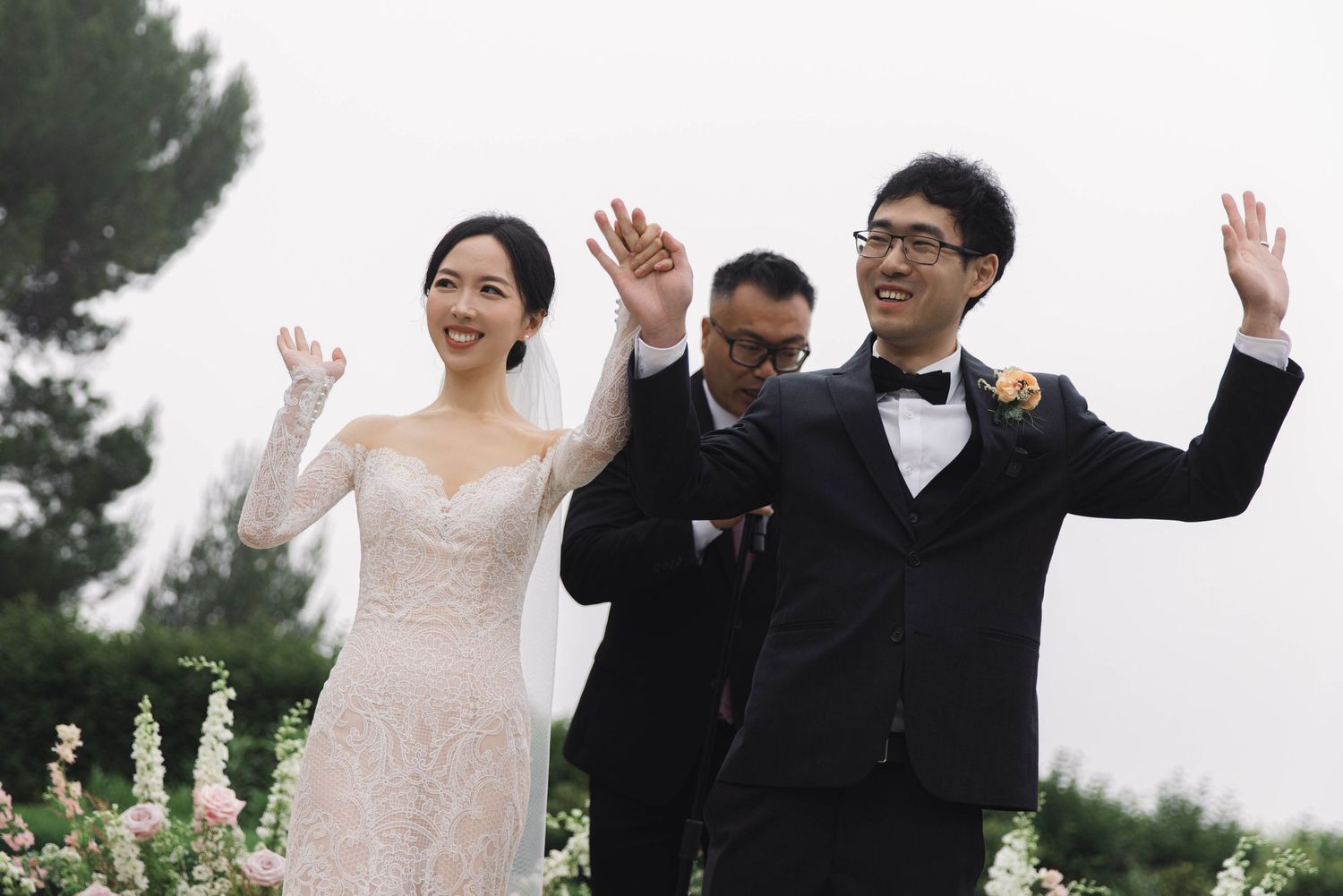Wedding party members celebrate with raised arms on a stone patio during festivities.