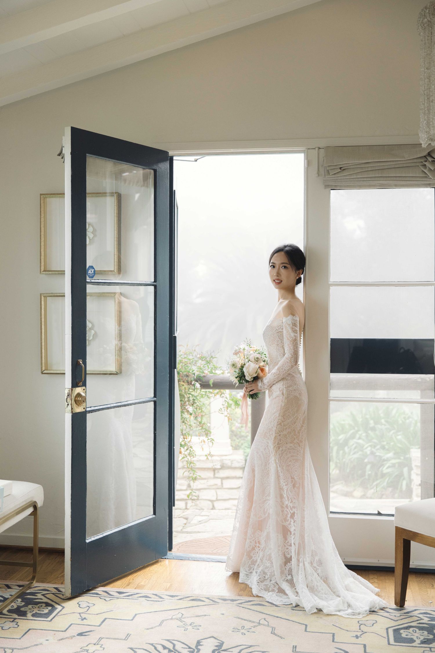 A flowing white lace wedding gown is displayed against modern interior with geometric patterned floor.