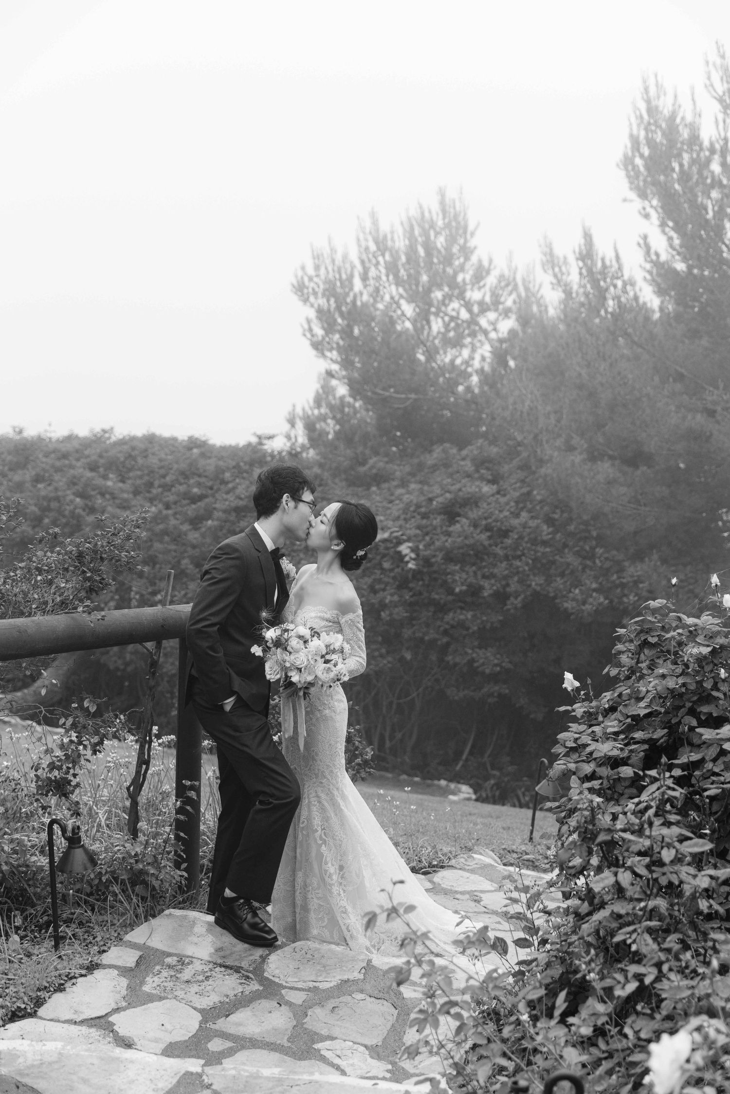 Black and white photo of wedding couple sharing tender moment in garden with stone path.